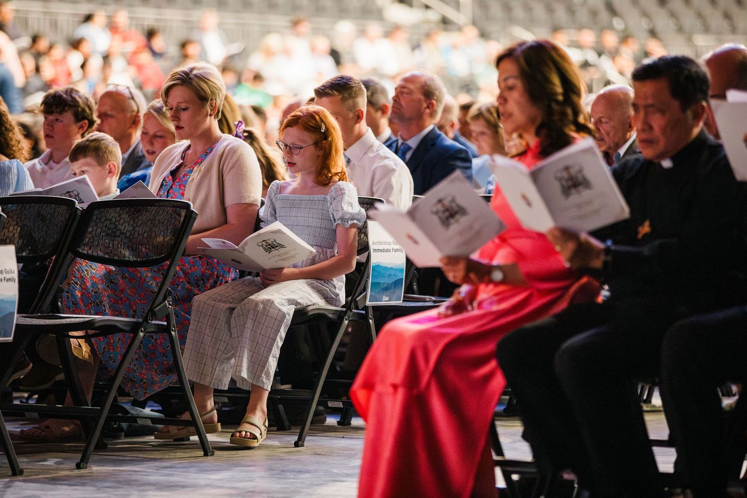 A large choir group performs together while reading from sheet music in an auditorium setting.