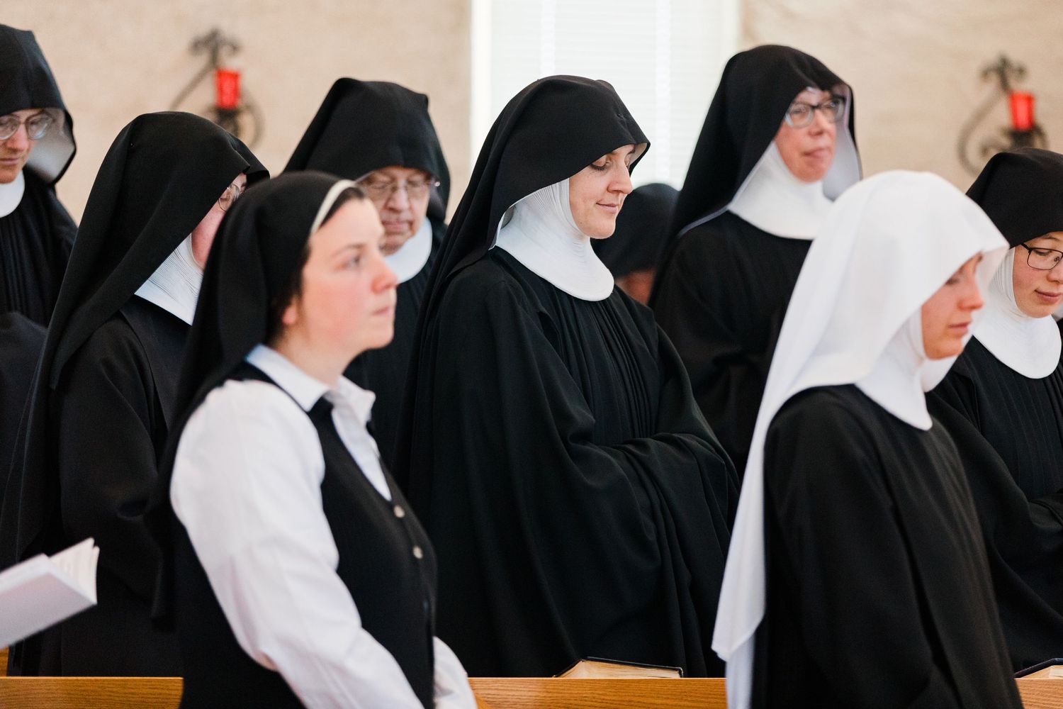 Catholic nuns in traditional black and white habits standing together in a church during a religious ceremony.