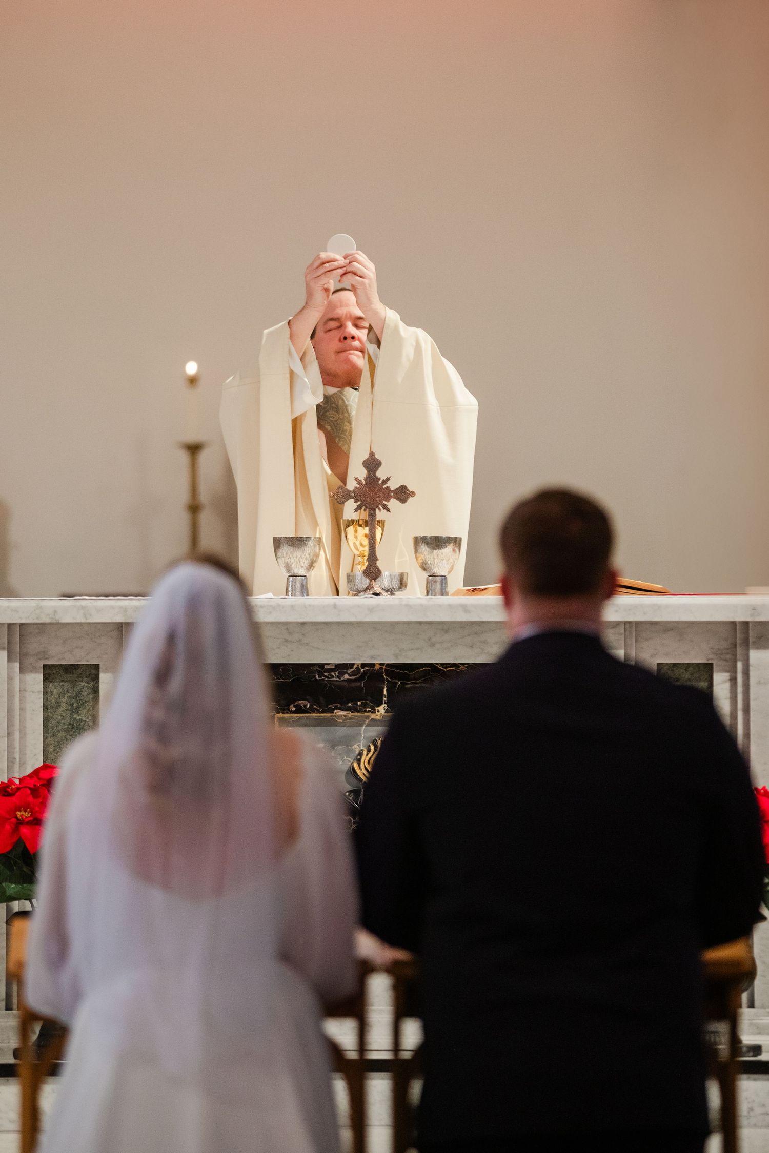 A Catholic wedding ceremony shows a priest at the altar with a bride and groom silhouetted in the foreground.