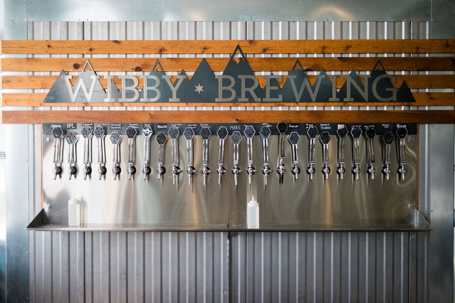 Long row of silver beer taps at a brewery bar with multiple draft lines.
