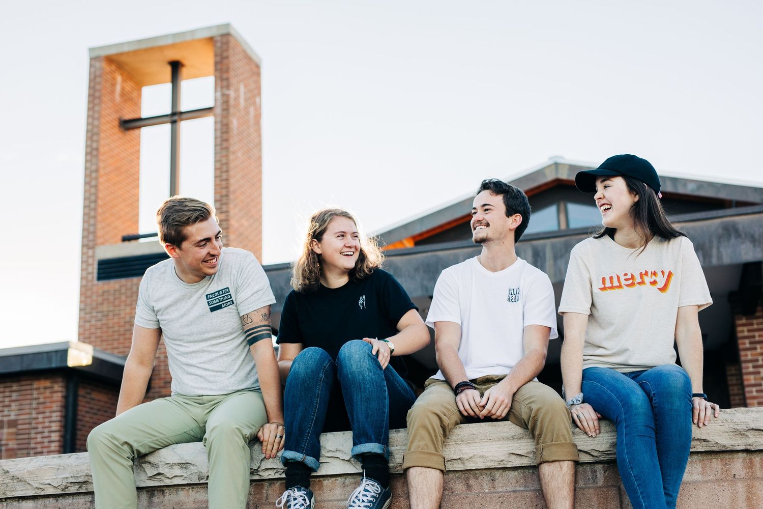 Group of people sitting and laughing together on a rooftop or outdoor area with brick walls in the background.