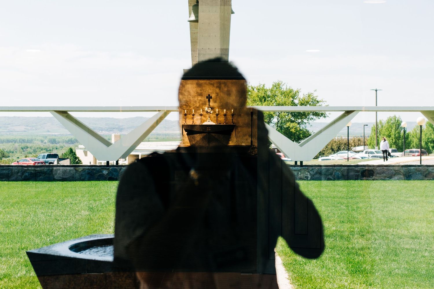 Someone in a dark coat stands in front of a garden setting on a sunny day.