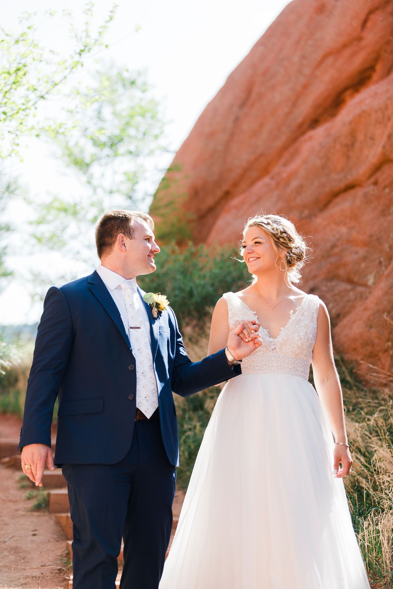 Bride and groom walk hand in hand among red rock formations in Colorado on their wedding day.