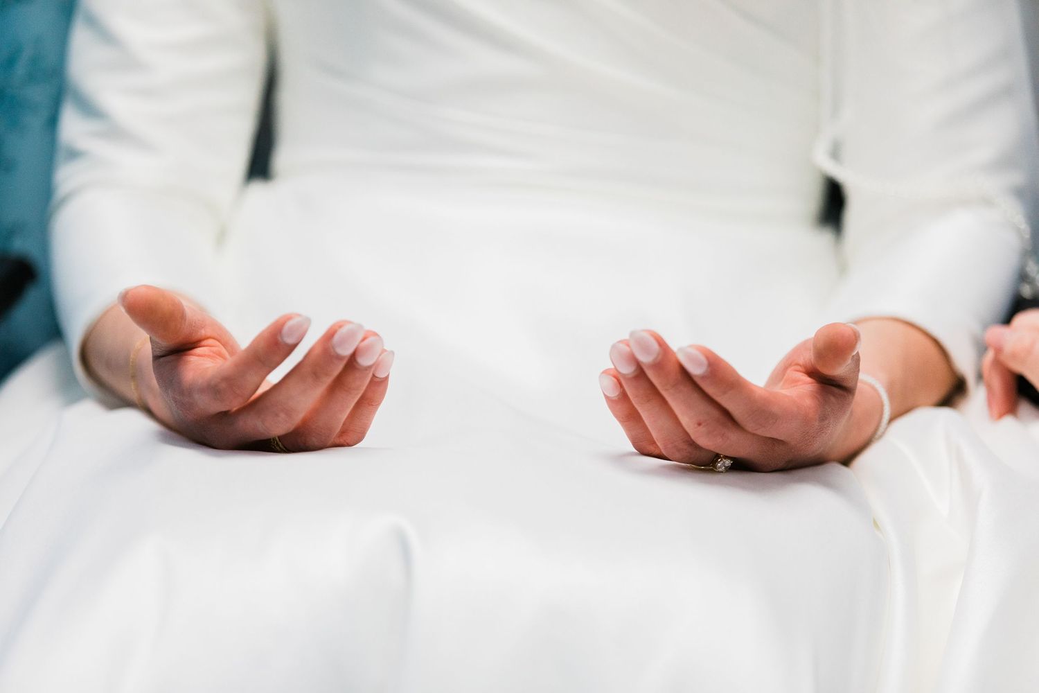 Close-up of a bride's hands with French manicure resting on her white wedding dress.