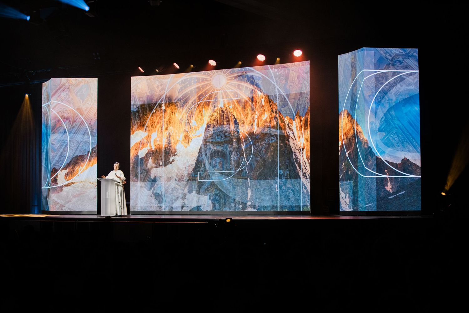 Large digital art displays show mountain landscapes on stage with dramatic lighting and artistic projections.