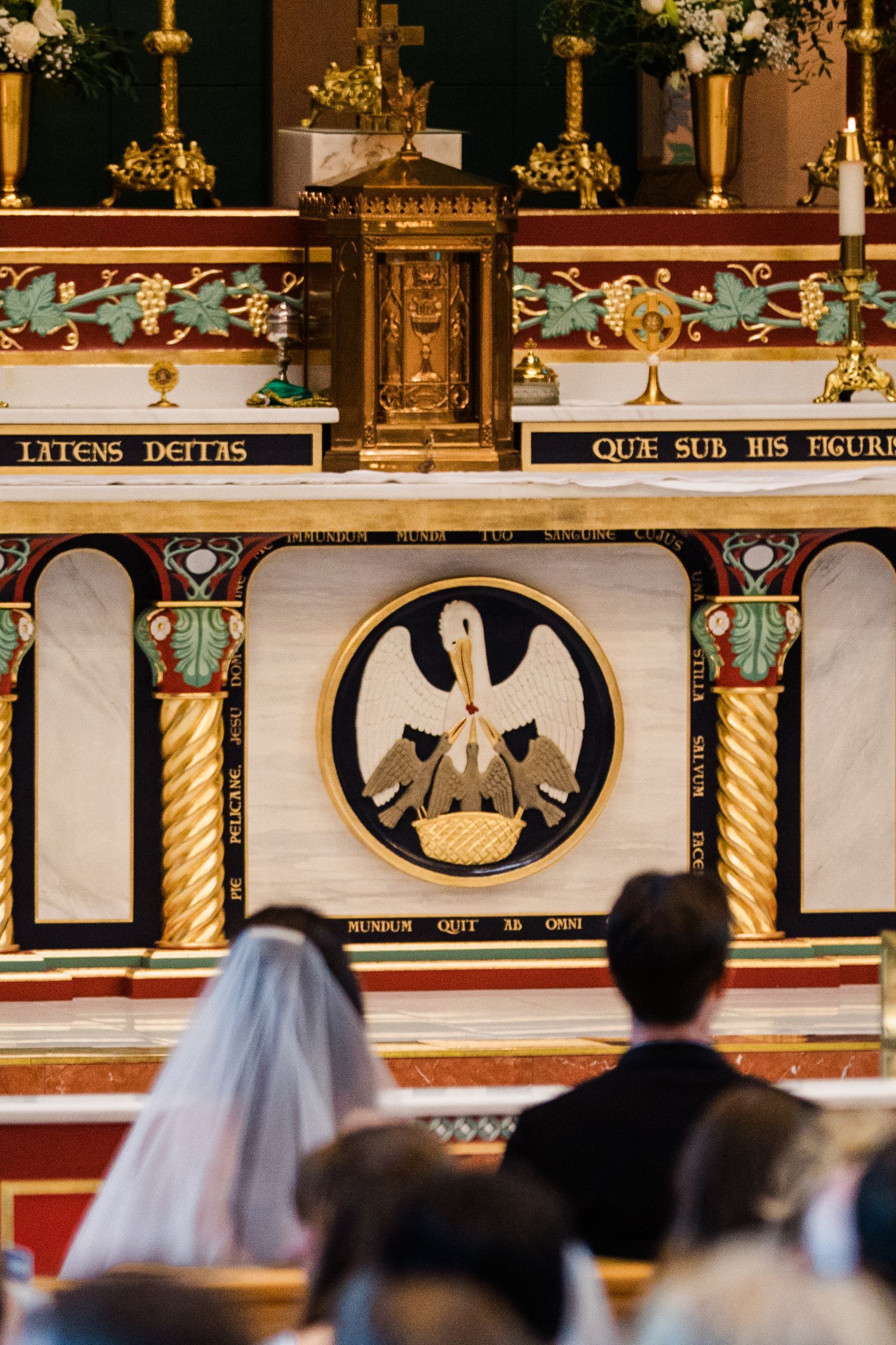 Wedding ceremony at an ornate church altar featuring a golden tabernacle and pelican religious symbol in circular medallion.