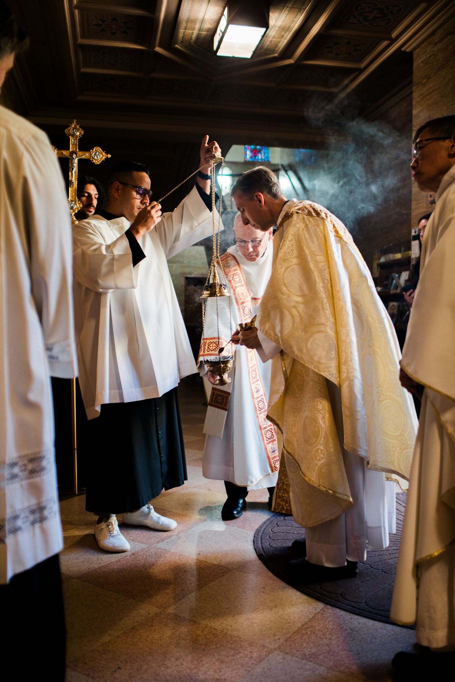 Catholic clergy in ornate vestments perform a religious ceremony with incense in a church.