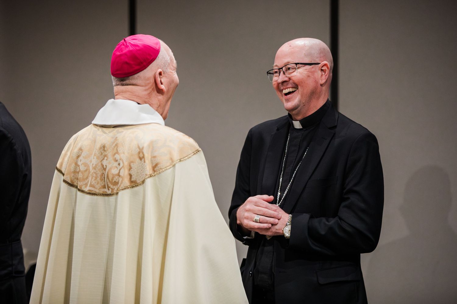 Catholic clergy members in traditional religious attire greet each other warmly during a formal gathering.