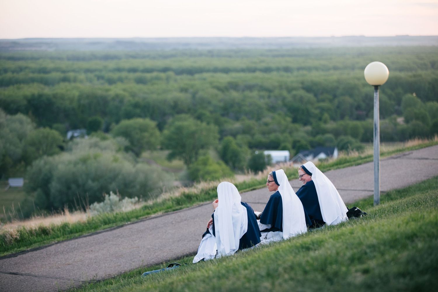 A panoramic series of photos showing people sitting on a grassy hill watching a sunset over a vast landscape.