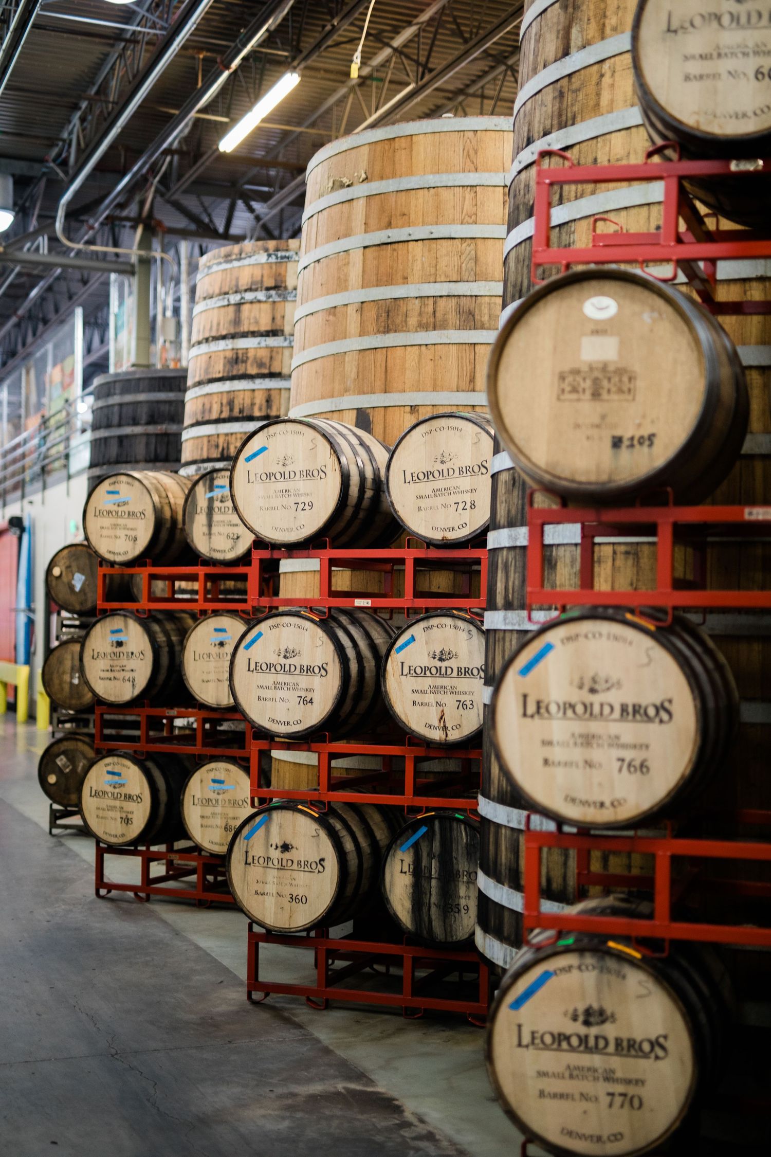 Wooden whiskey barrels stacked on red metal racks in a distillery warehouse.