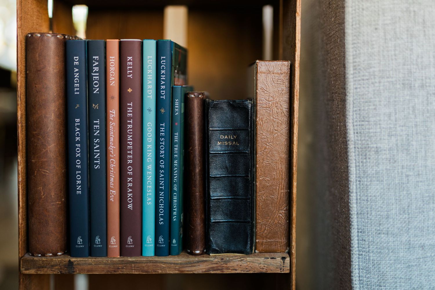 Vintage leather-bound books arranged neatly on a wooden bookshelf in warm lighting.