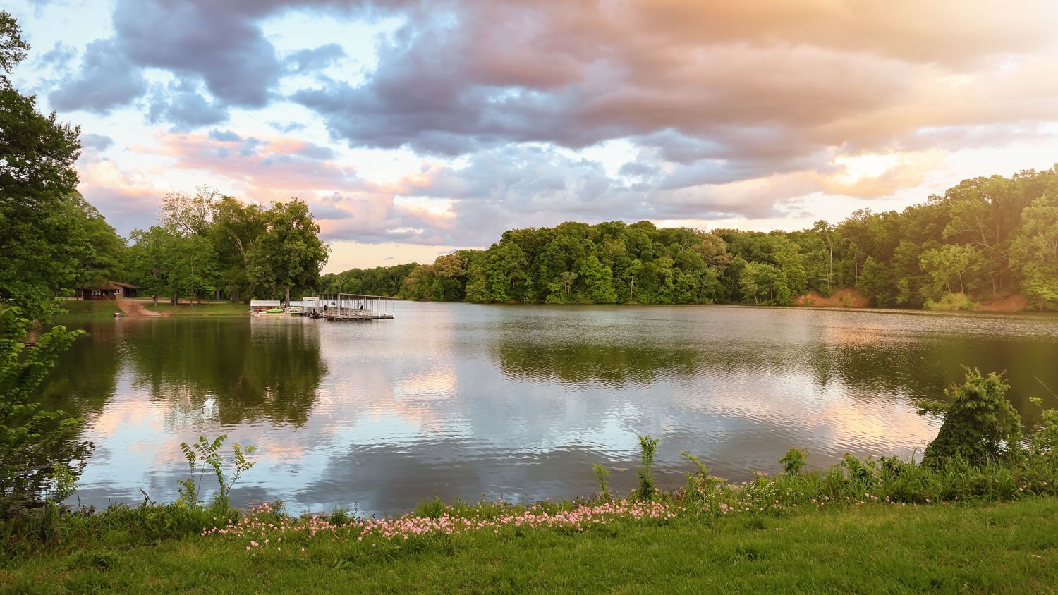 Peaceful lake at sunset with pink clouds reflecting on calm waters.