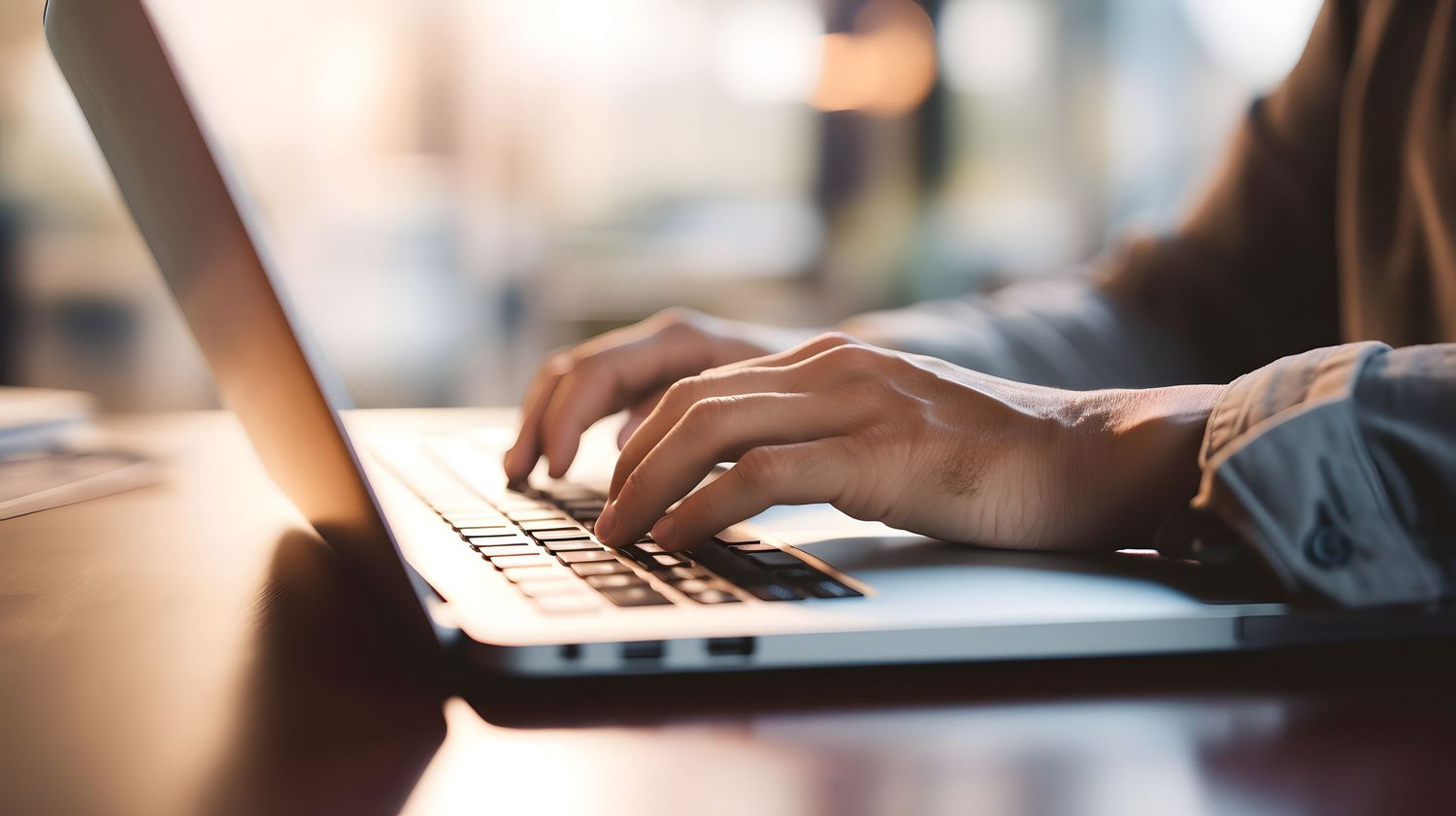 Close-up of hands typing on laptop keyboard in office setting.