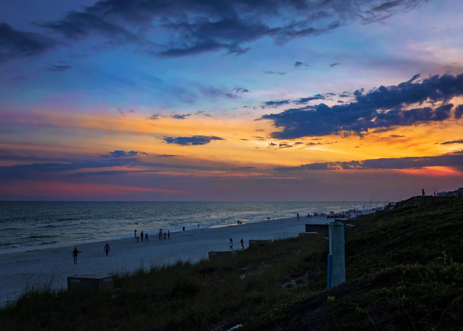 Vibrant sunset over ocean beach with silhouetted people and colorful sky.