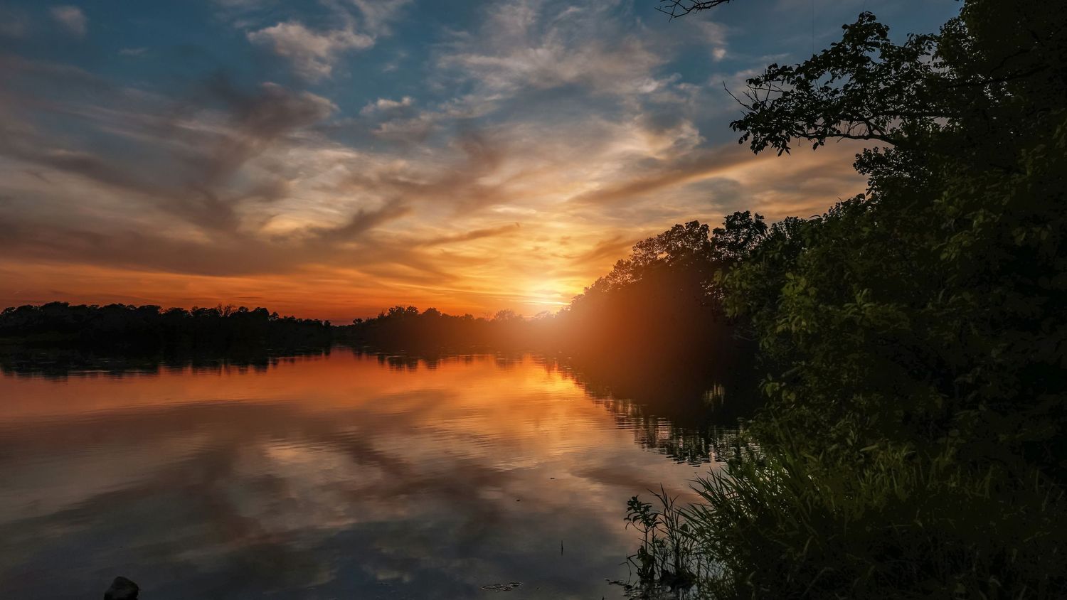 Dramatic sunset over a lake with silhouetted trees and reflective water.