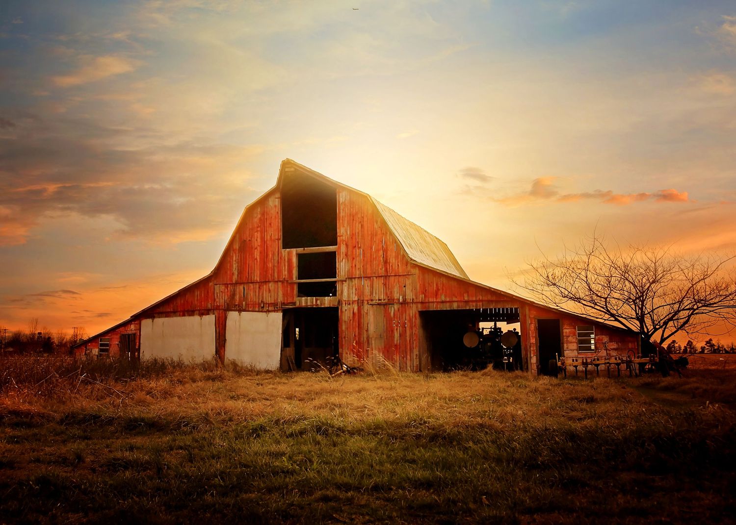 Old red barn silhouetted against a dramatic orange sunset sky.