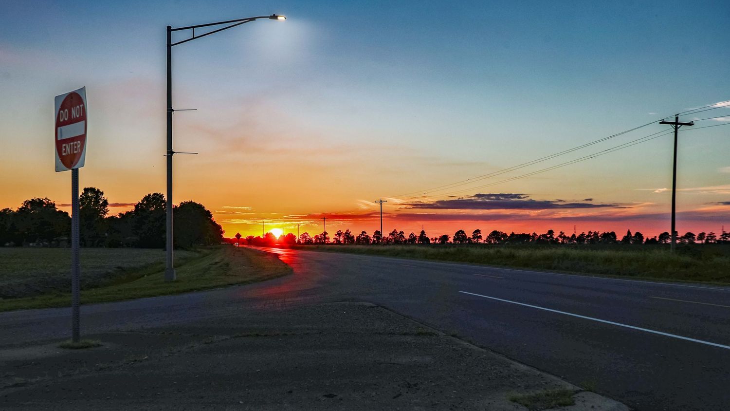 Stunning sunset over a rural road with a street lamp and stop sign silhouetted against the colorful sky.