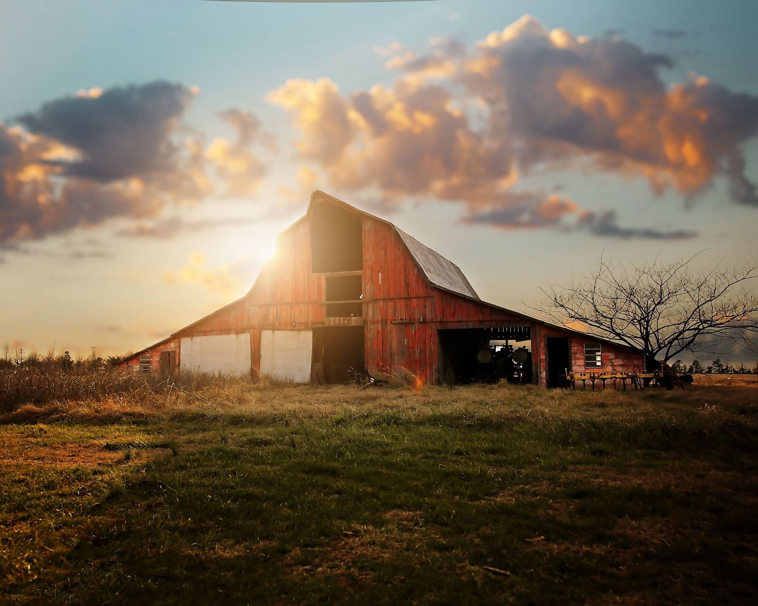 Rustic red barn glowing in golden sunset light with dramatic orange clouds overhead.