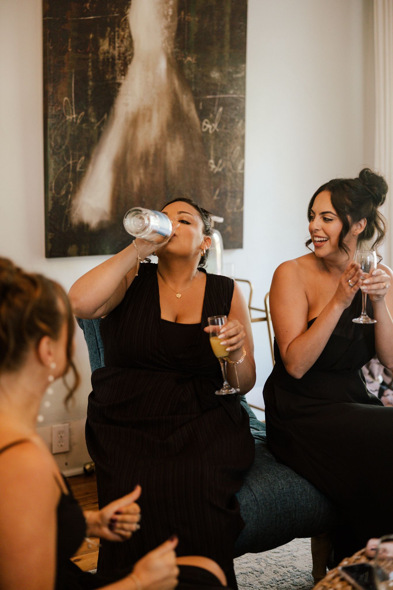 Wedding guests in black dresses laugh and celebrate with wine glasses at a reception.