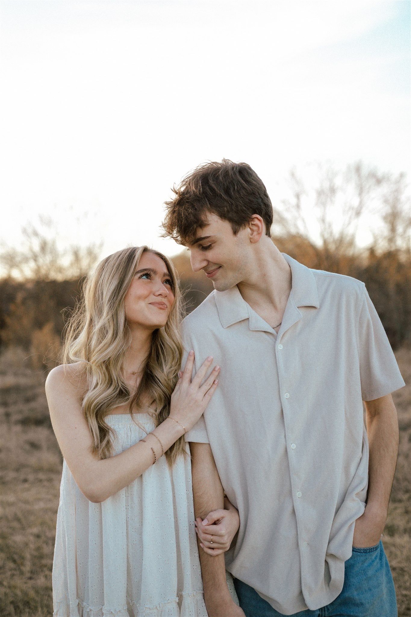 Romantic couple poses in a desert setting during golden hour wearing light colored clothing.