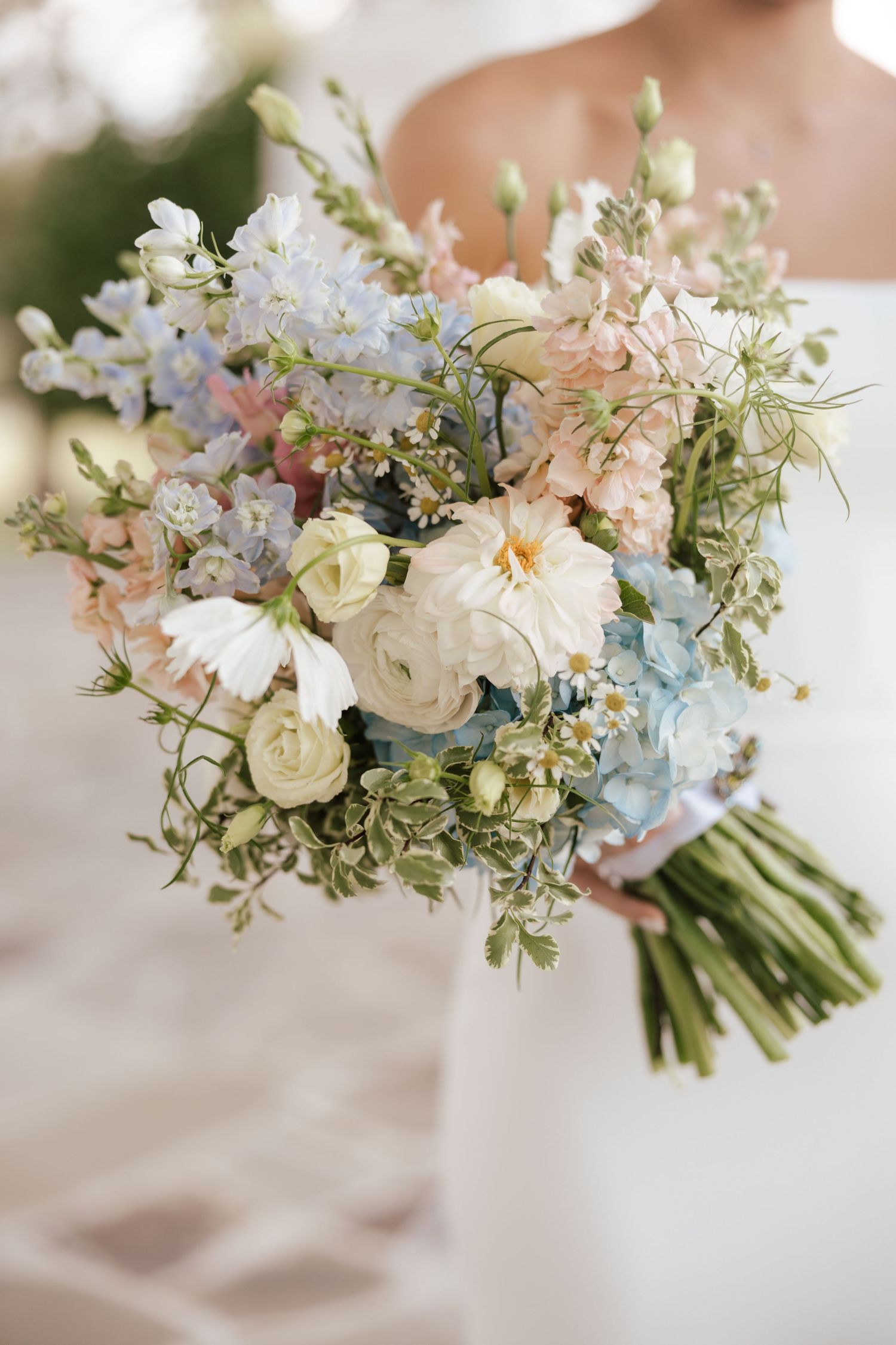 Delicate white and blue wedding bouquet featuring roses, hydrangeas, and wispy greenery tied with ribbon.