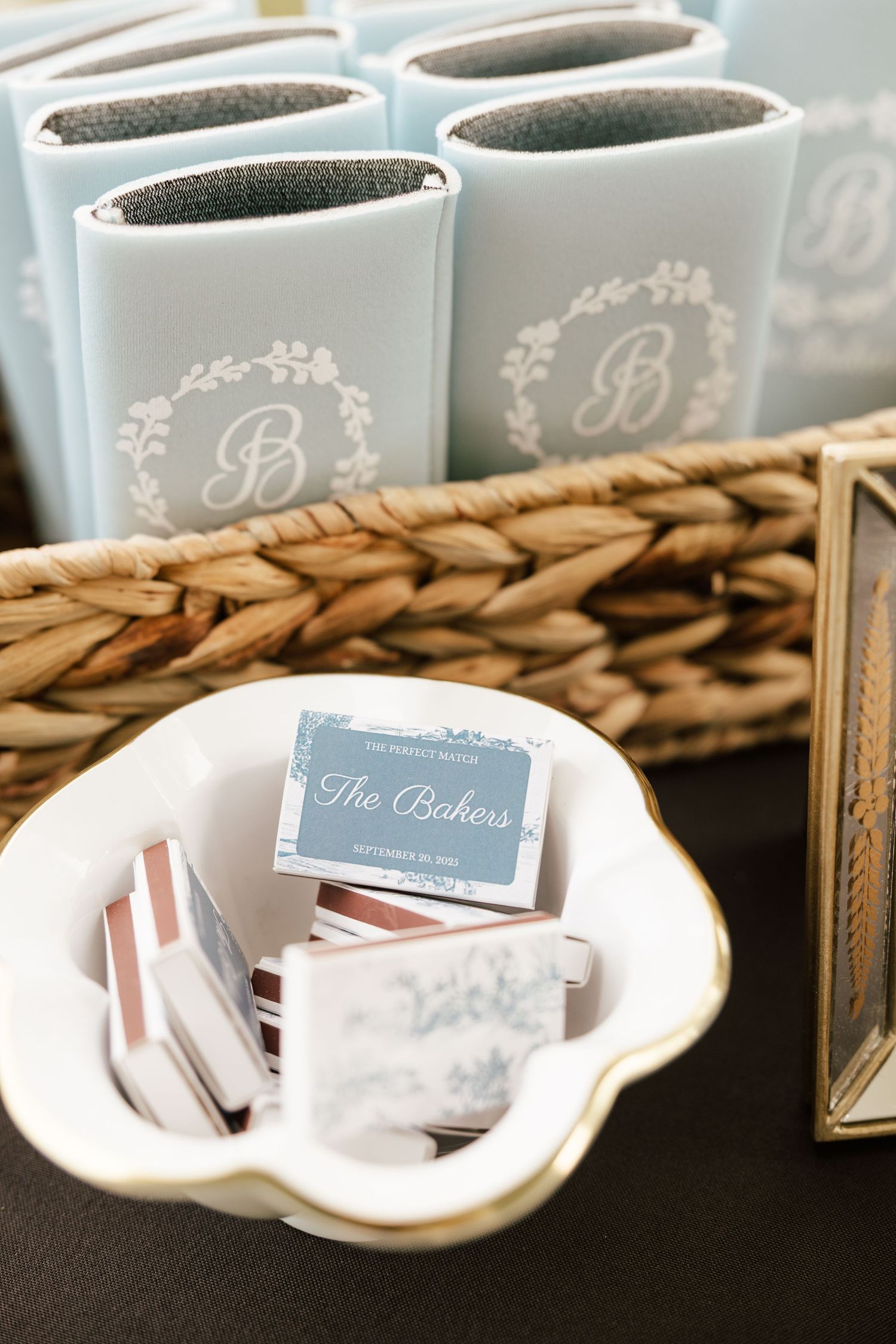 Custom monogrammed light blue koozies and personalized matchboxes displayed as wedding guest favors.
