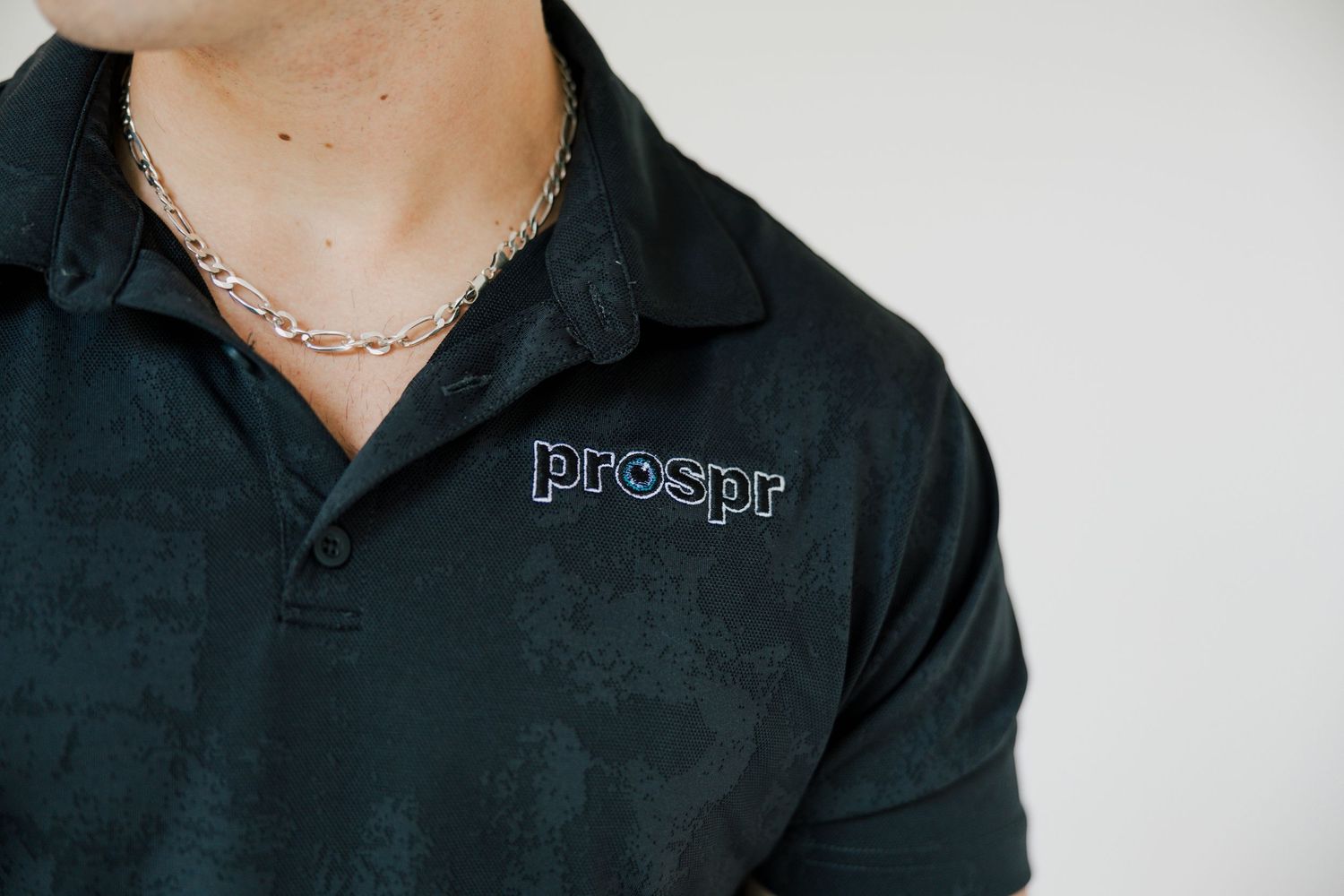 Close-up details of black polo shirt with embroidered logo and accessories.
