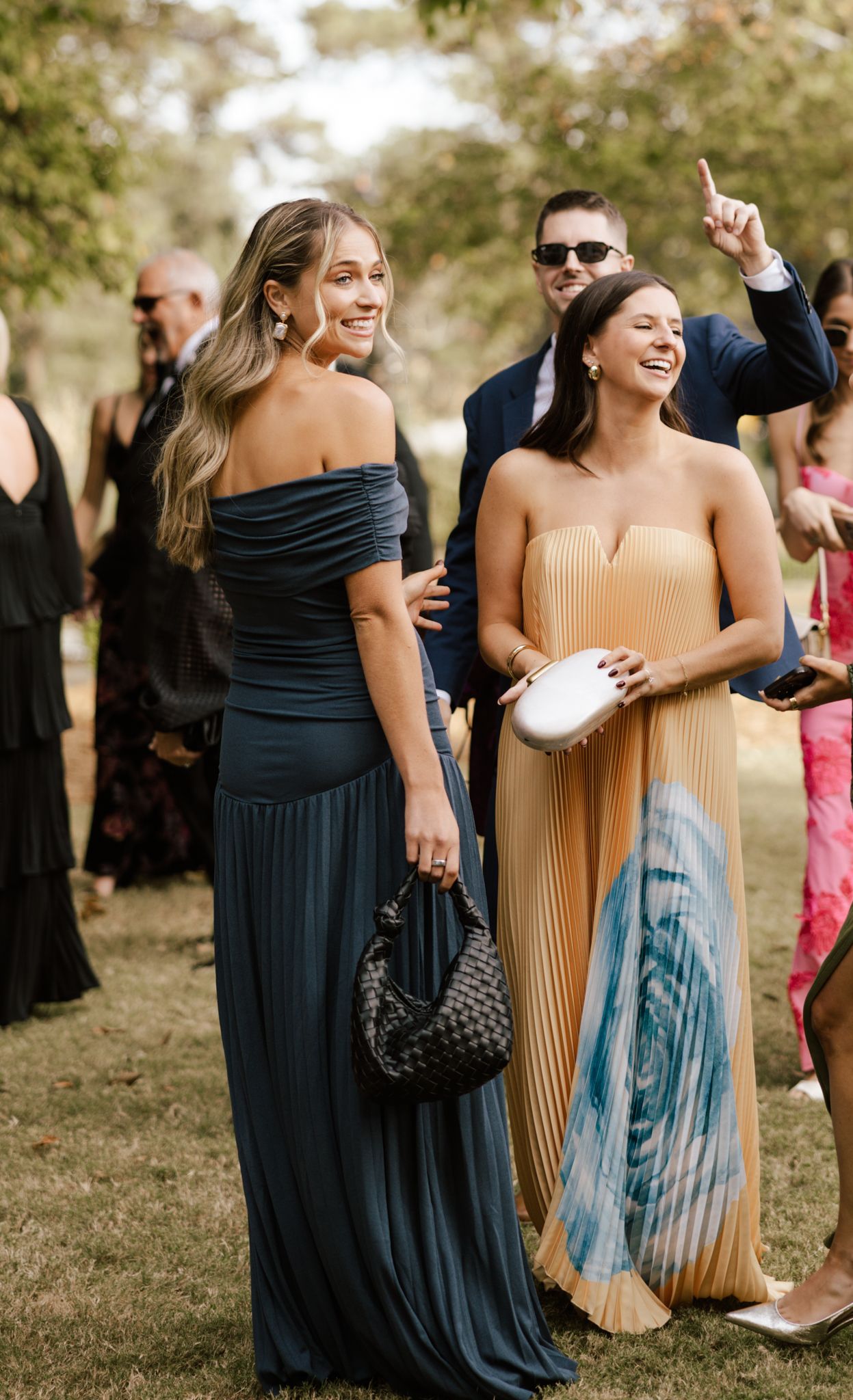 Wedding guests in formal dresses laughing and celebrating outdoors.