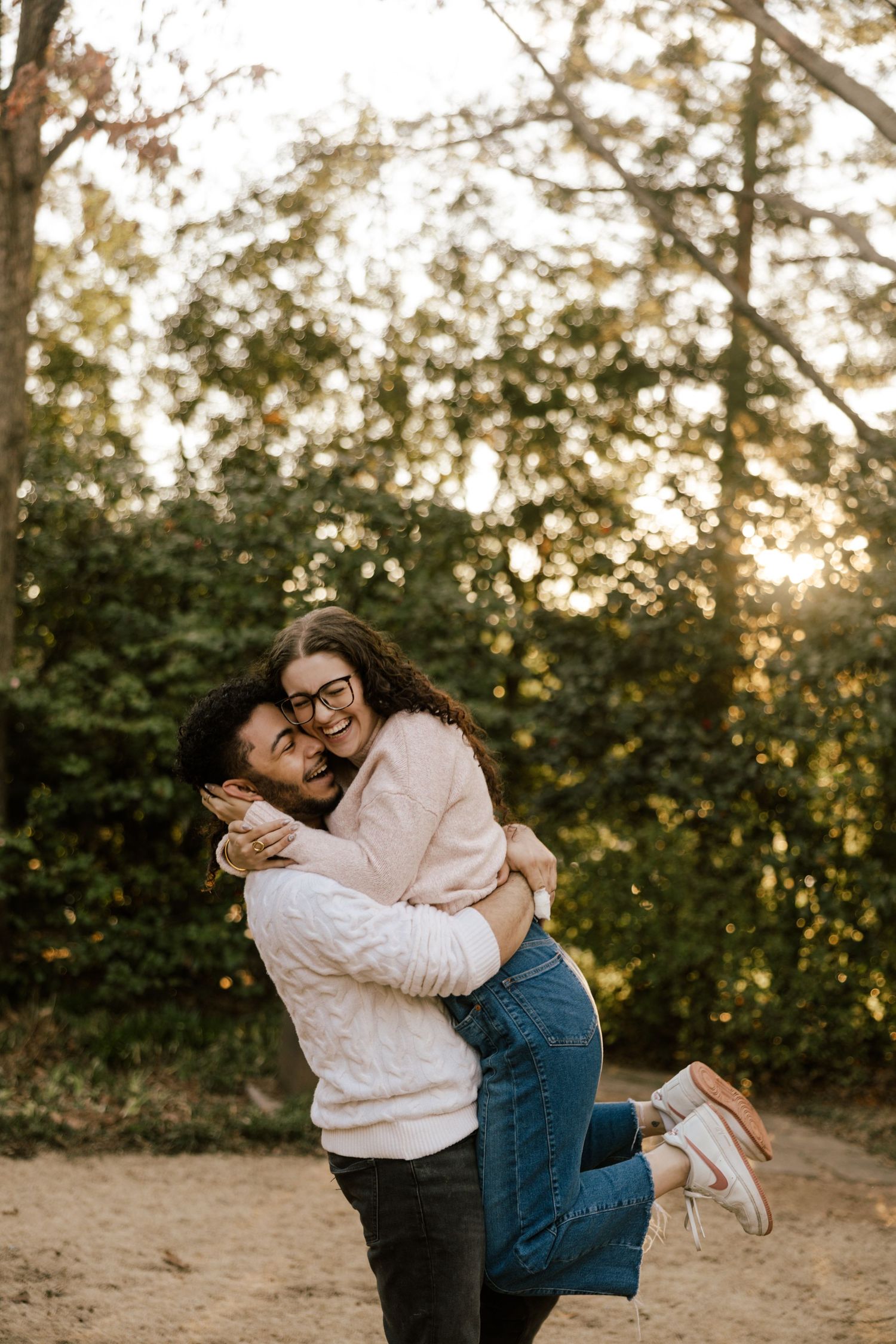 A couple embraces joyfully in an outdoor setting during golden hour with trees in the background.