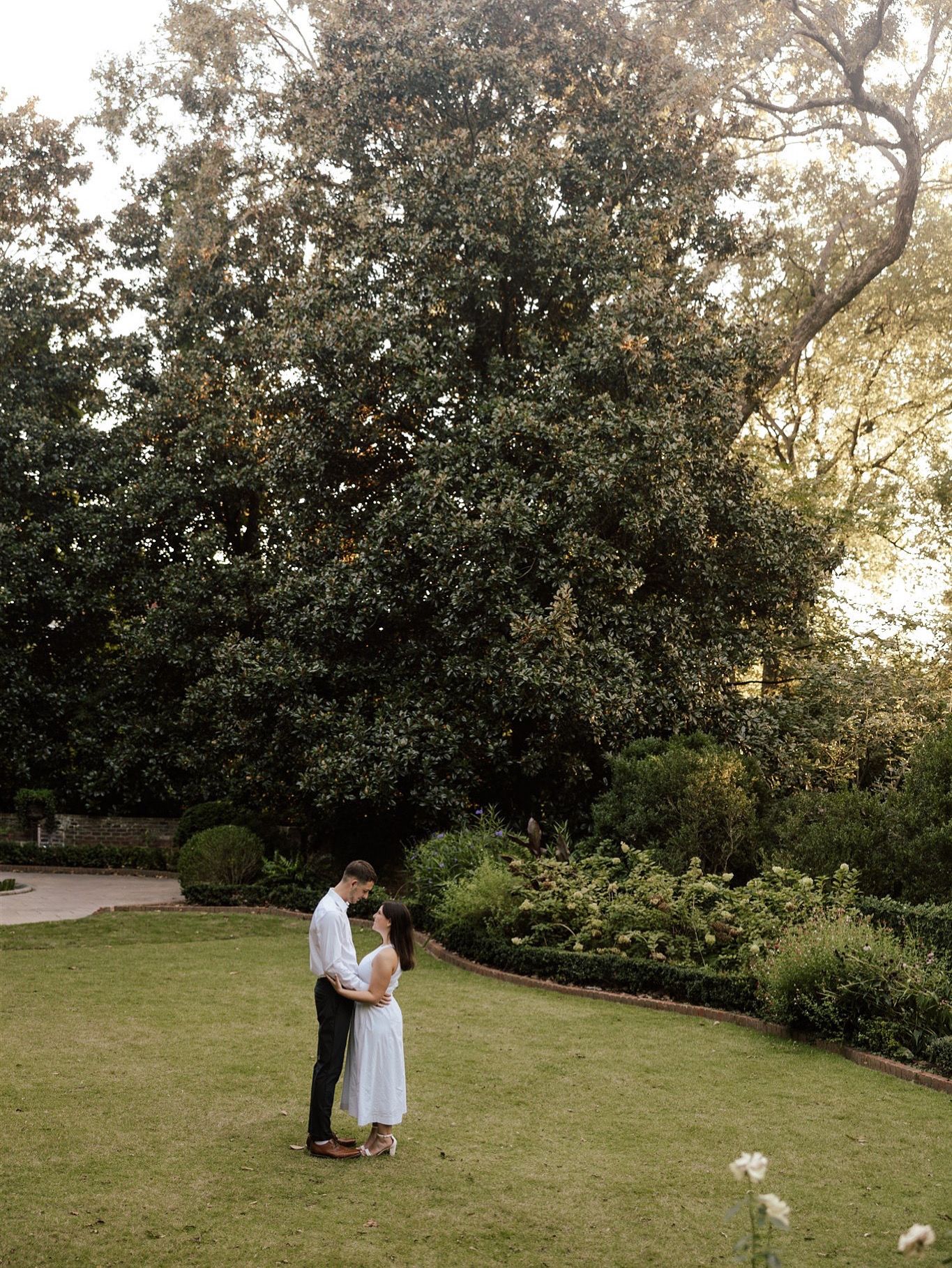 Romantic couple dancing together on a sunlit grassy lawn surrounded by trees.