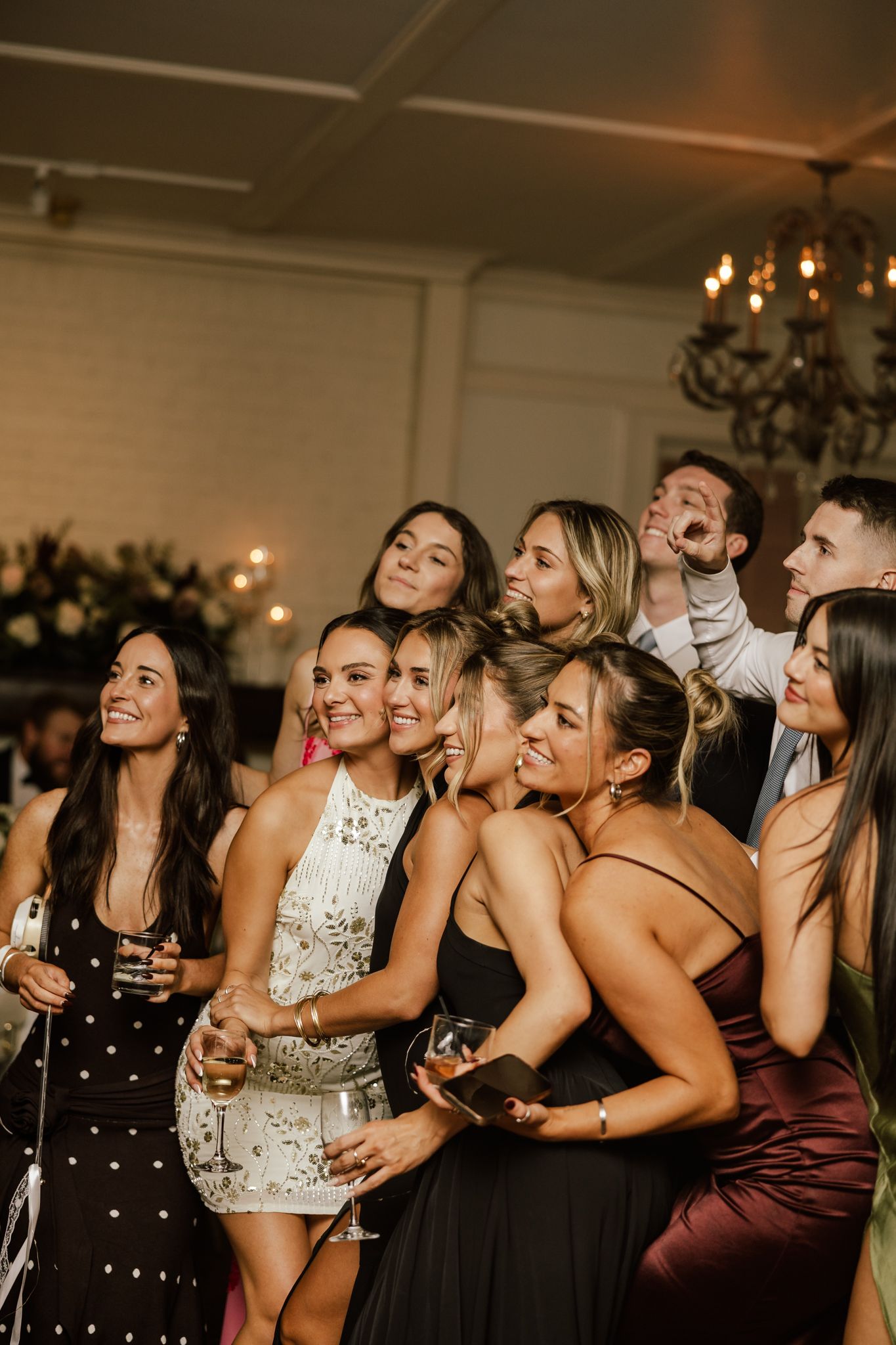A group of party guests laugh and pose together at an elegant indoor reception with chandelier lighting in Duluth Georgia