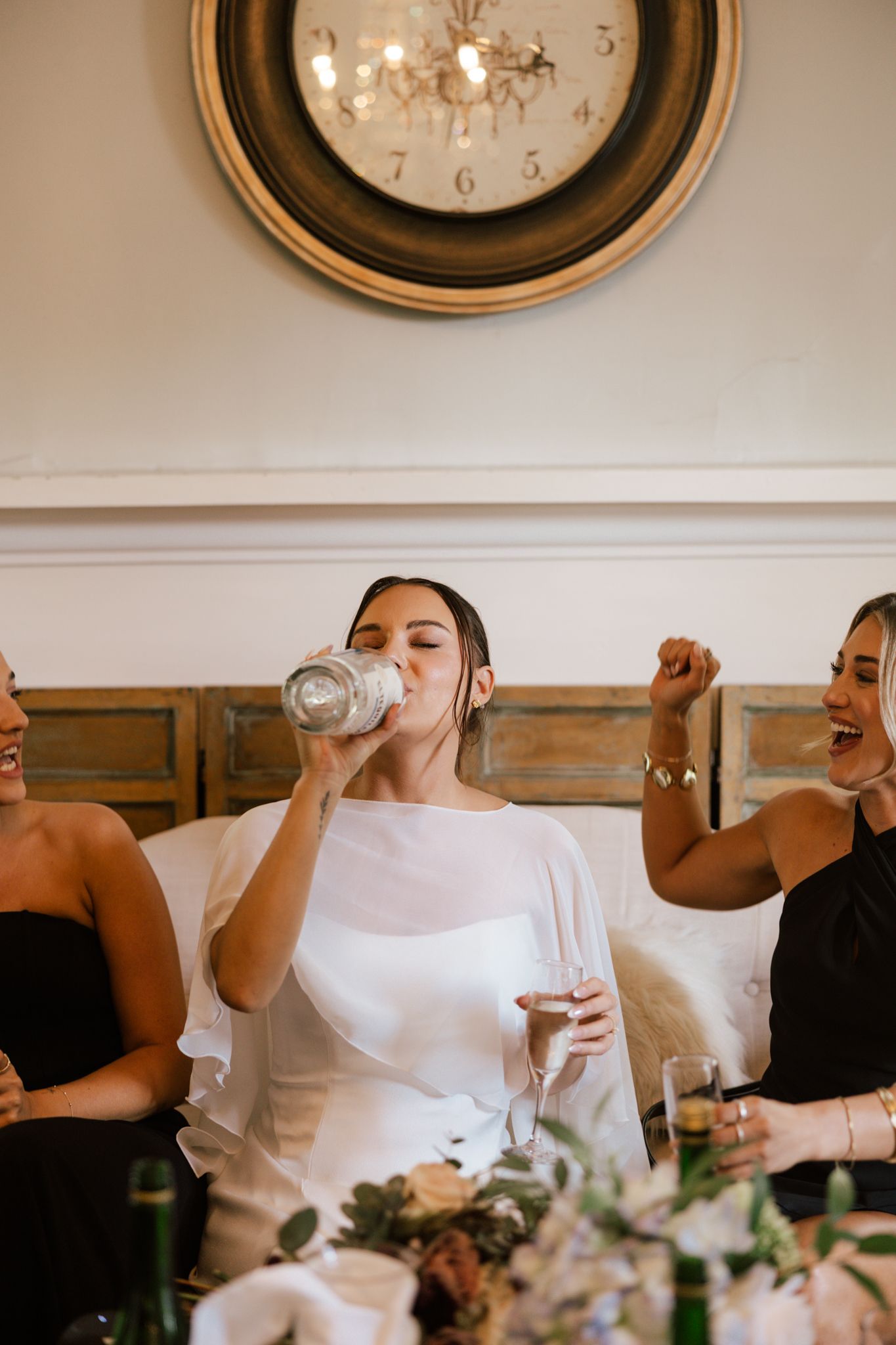 Wedding party members raise glasses for a celebratory toast under an ornate wall clock.