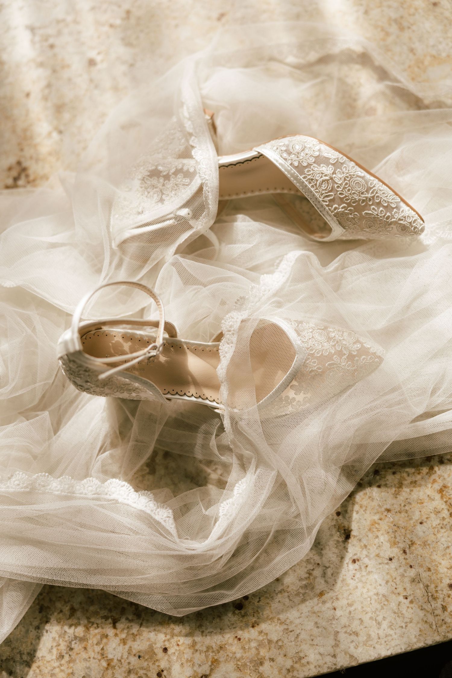 Delicate white tulle and lace wedding veil details laid out on a textured surface.