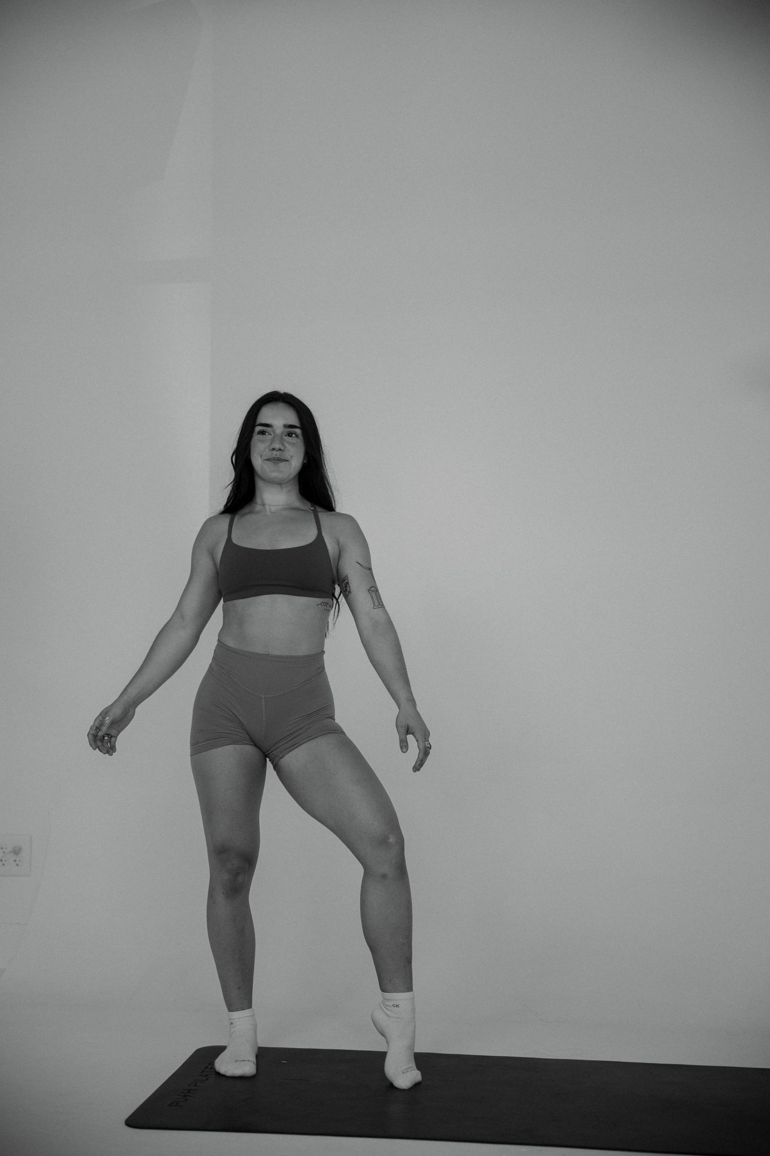 Athletic woman in gray workout set balancing on one leg on a yoga mat in black and white.