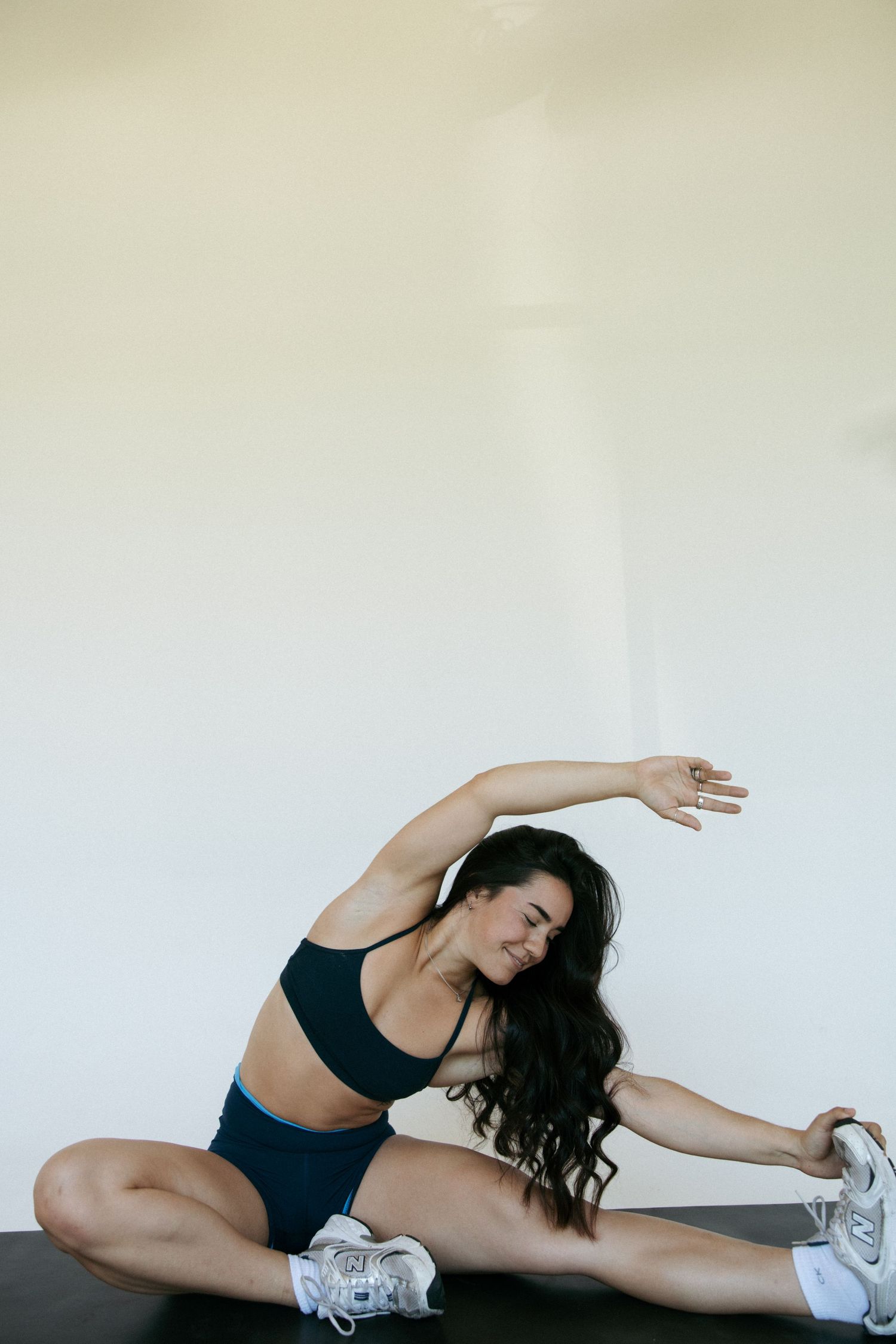 Fit woman in teal sports bra and shorts doing a seated side stretch on a gym mat.