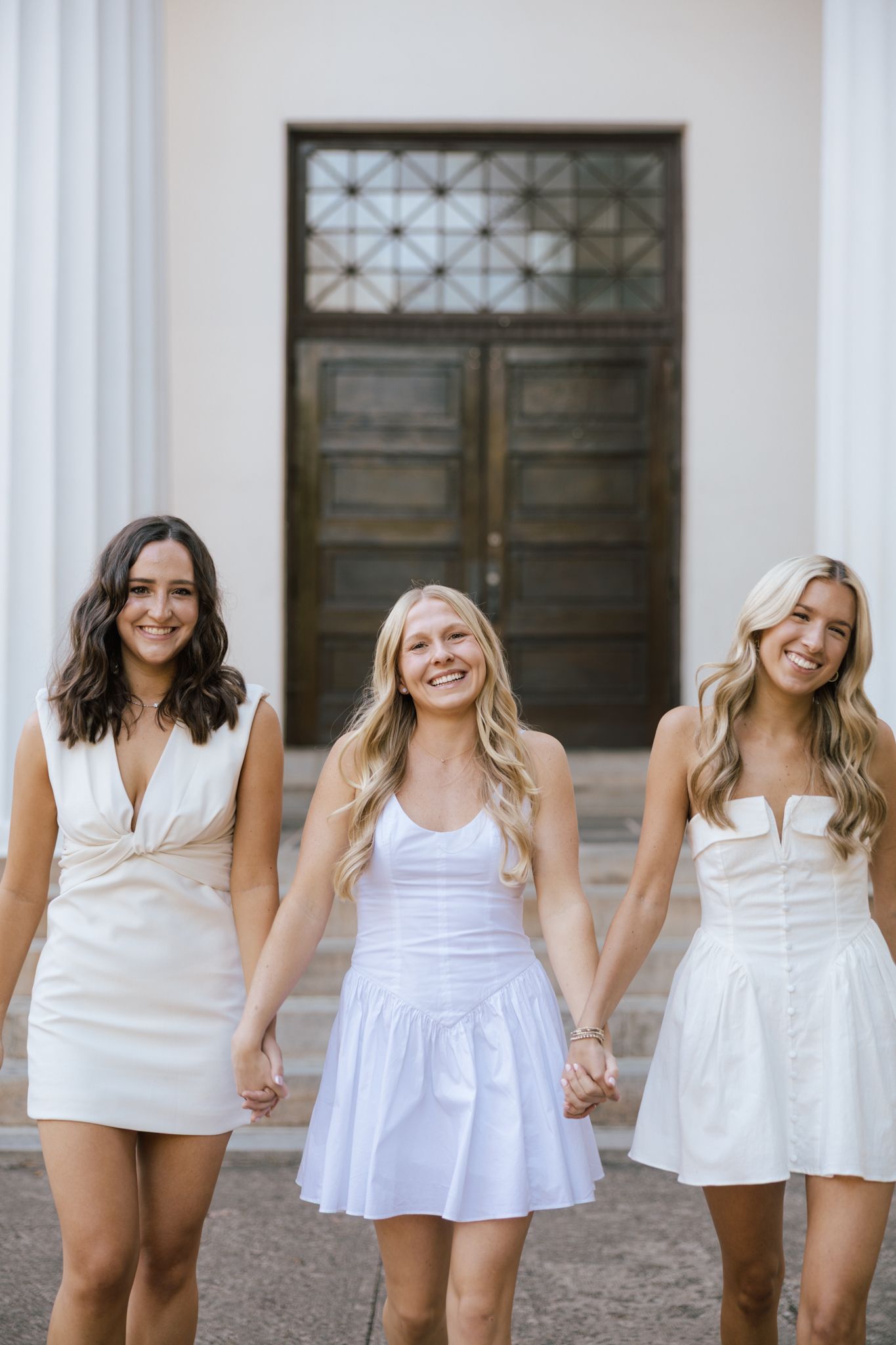 Cheerful group photo of graduates in white dresses posing together outdoors.