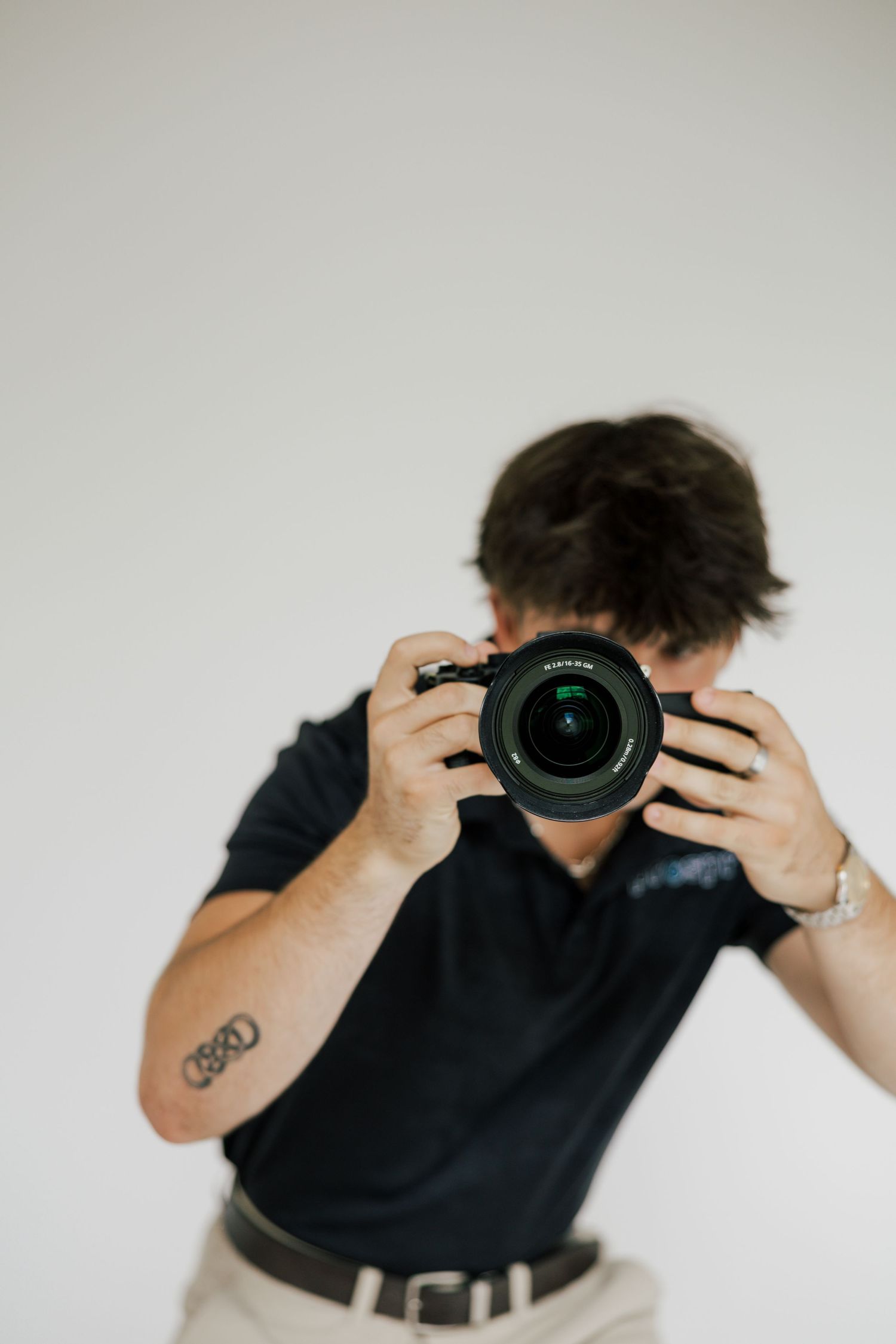 Photographer holding a professional camera with large lens against white background.