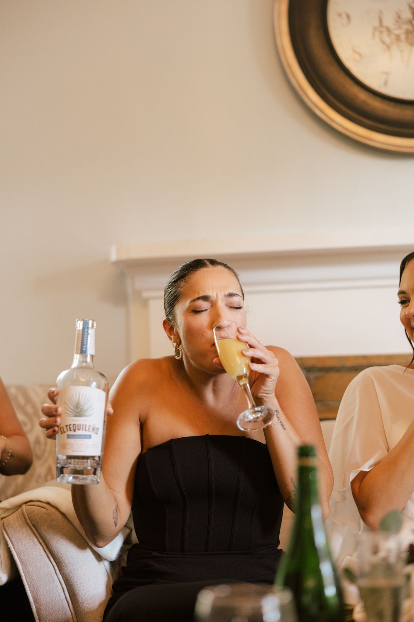 Wedding party members in black dresses drink from champagne glasses during celebrations.
