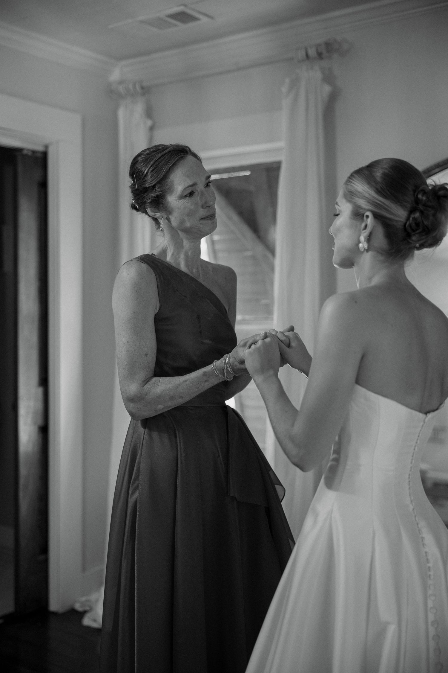 Black and white photo of a bride in a strapless gown holding hands with a woman in a one-shoulder dress.