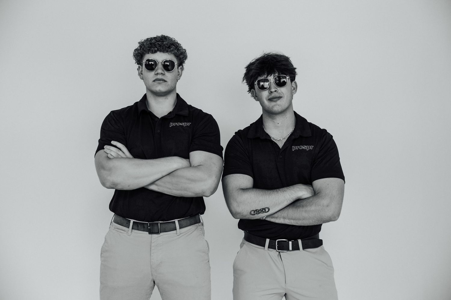 Two people in matching polo shirts and khakis pose confidently with sunglasses.