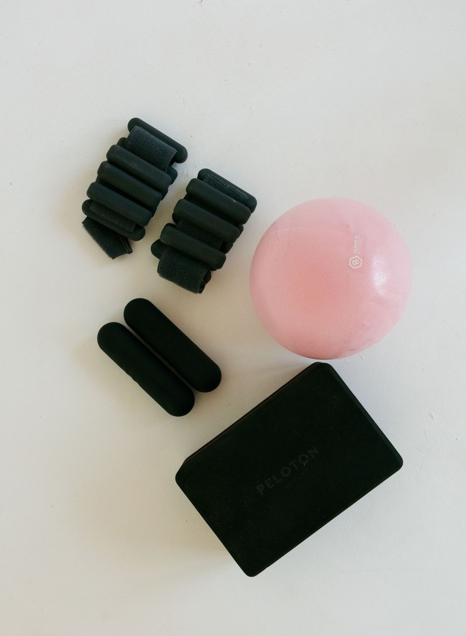 Pilates workout accessories including ankle weights, a pink ball, and a yoga block on white surface.