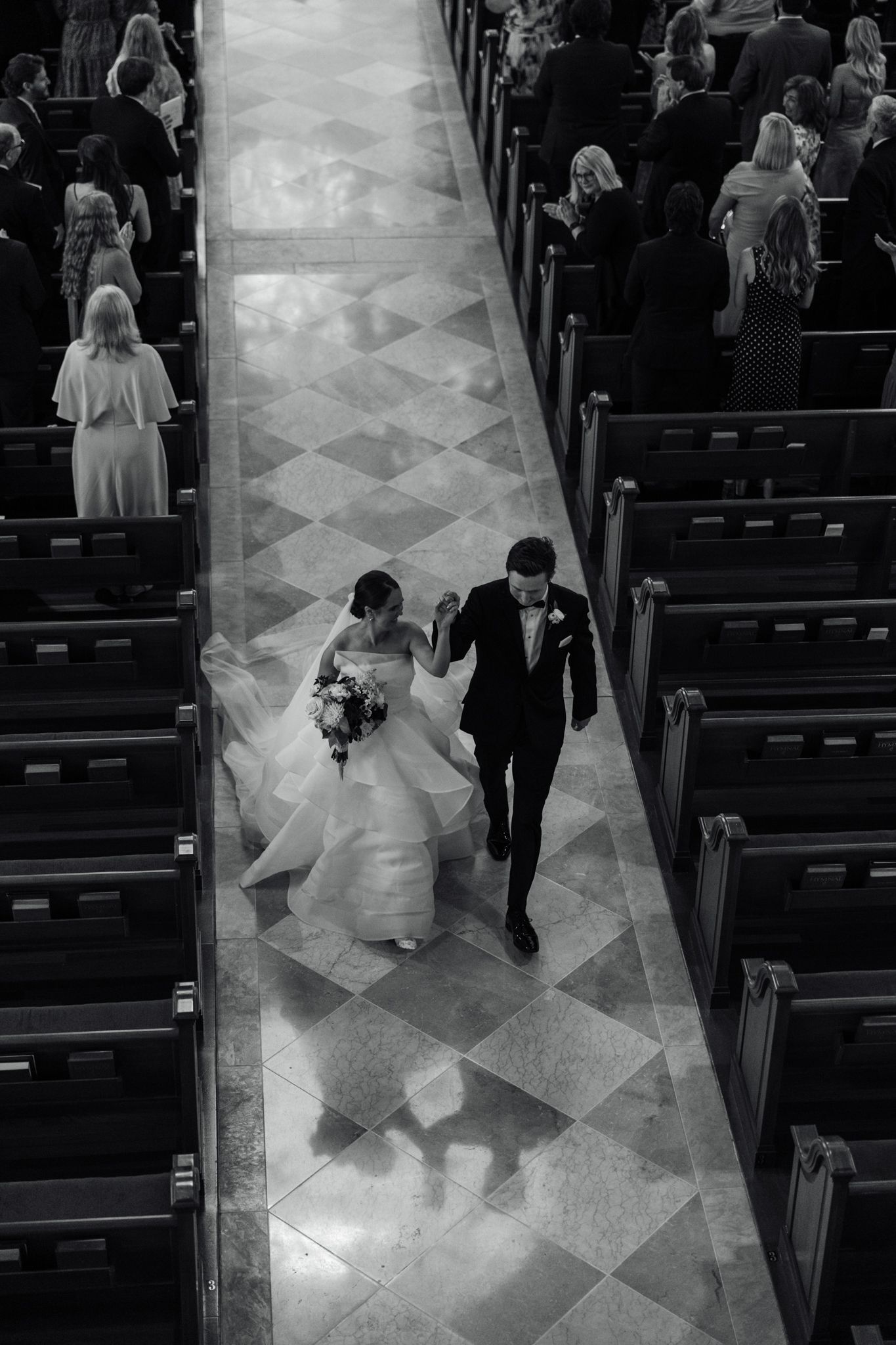 Black and white aerial view of bride and groom walking down church aisle after wedding ceremony.