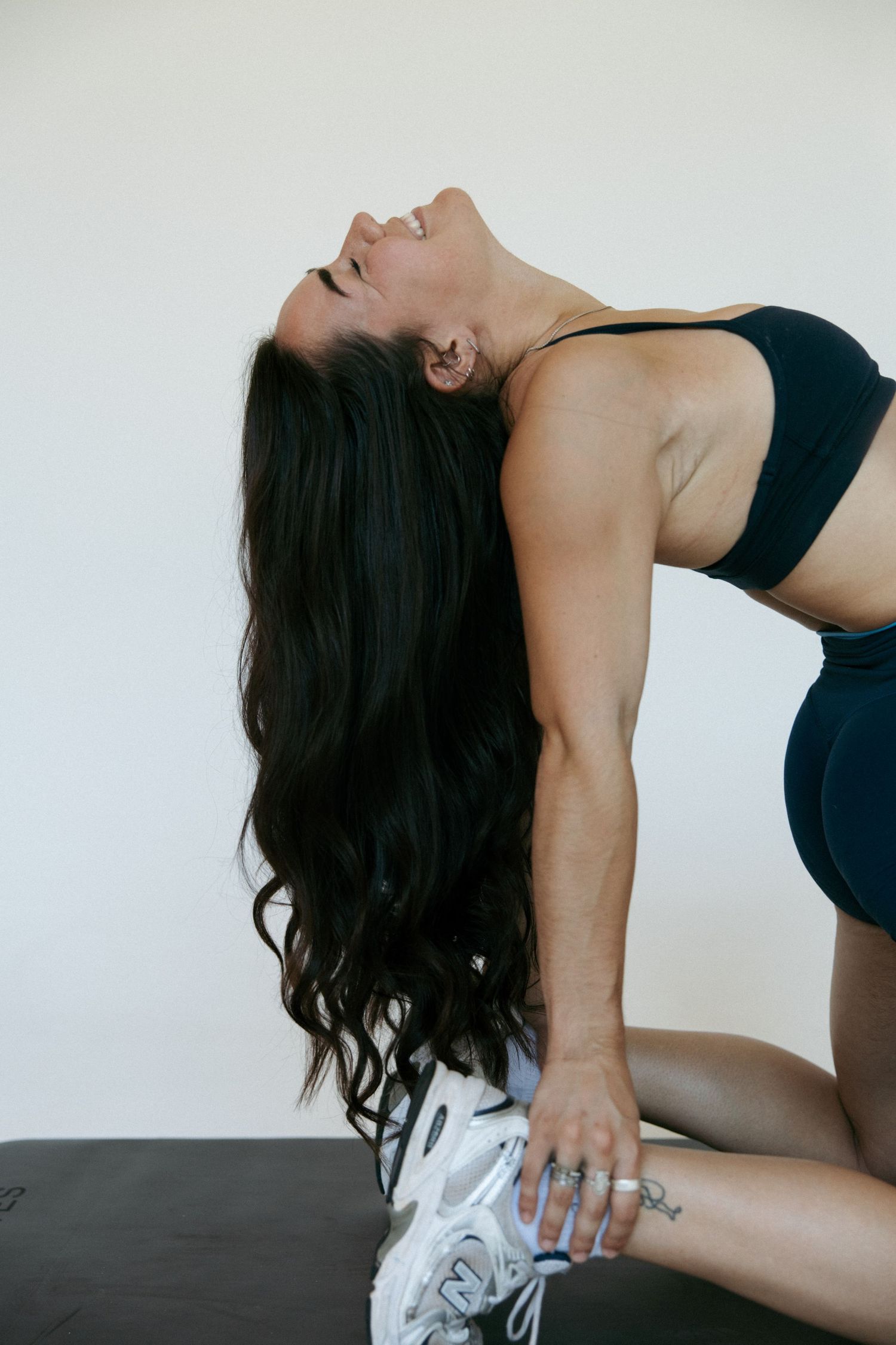Woman in black sports bra and leggings doing a backbend stretch on a yoga mat.