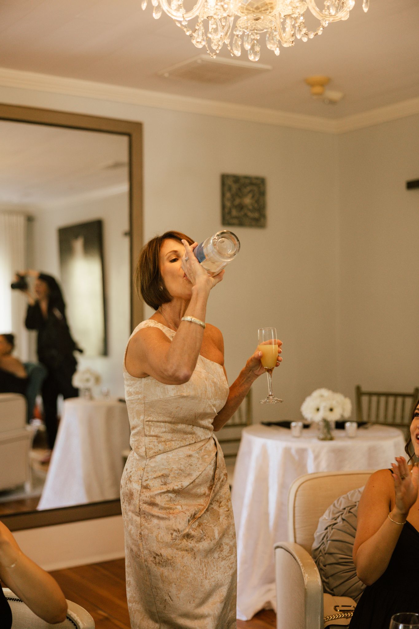 Bride in lace dress takes a celebratory drink in an elegant reception room.