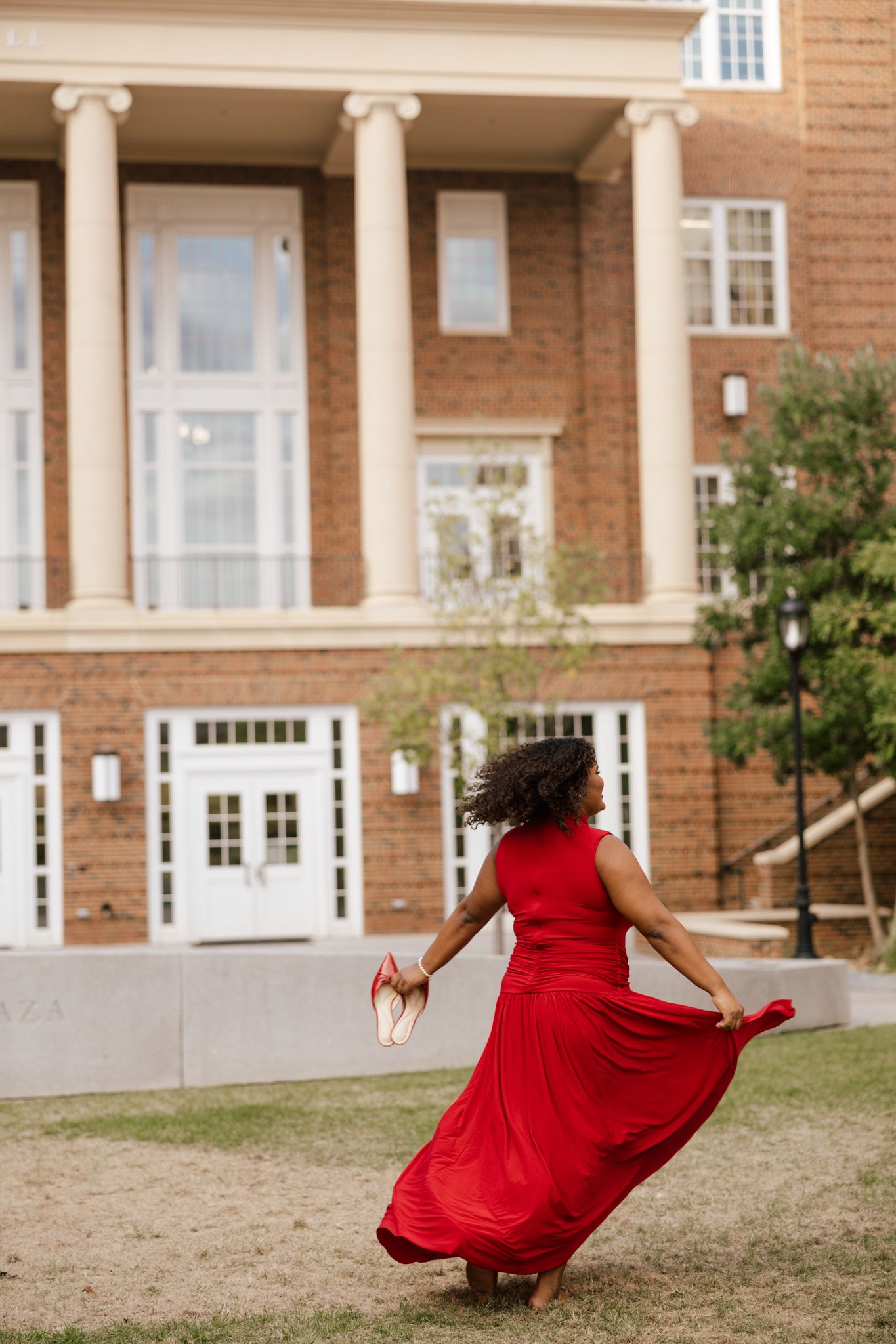 Figure in flowing red dress twirls in front of brick building with white columns.