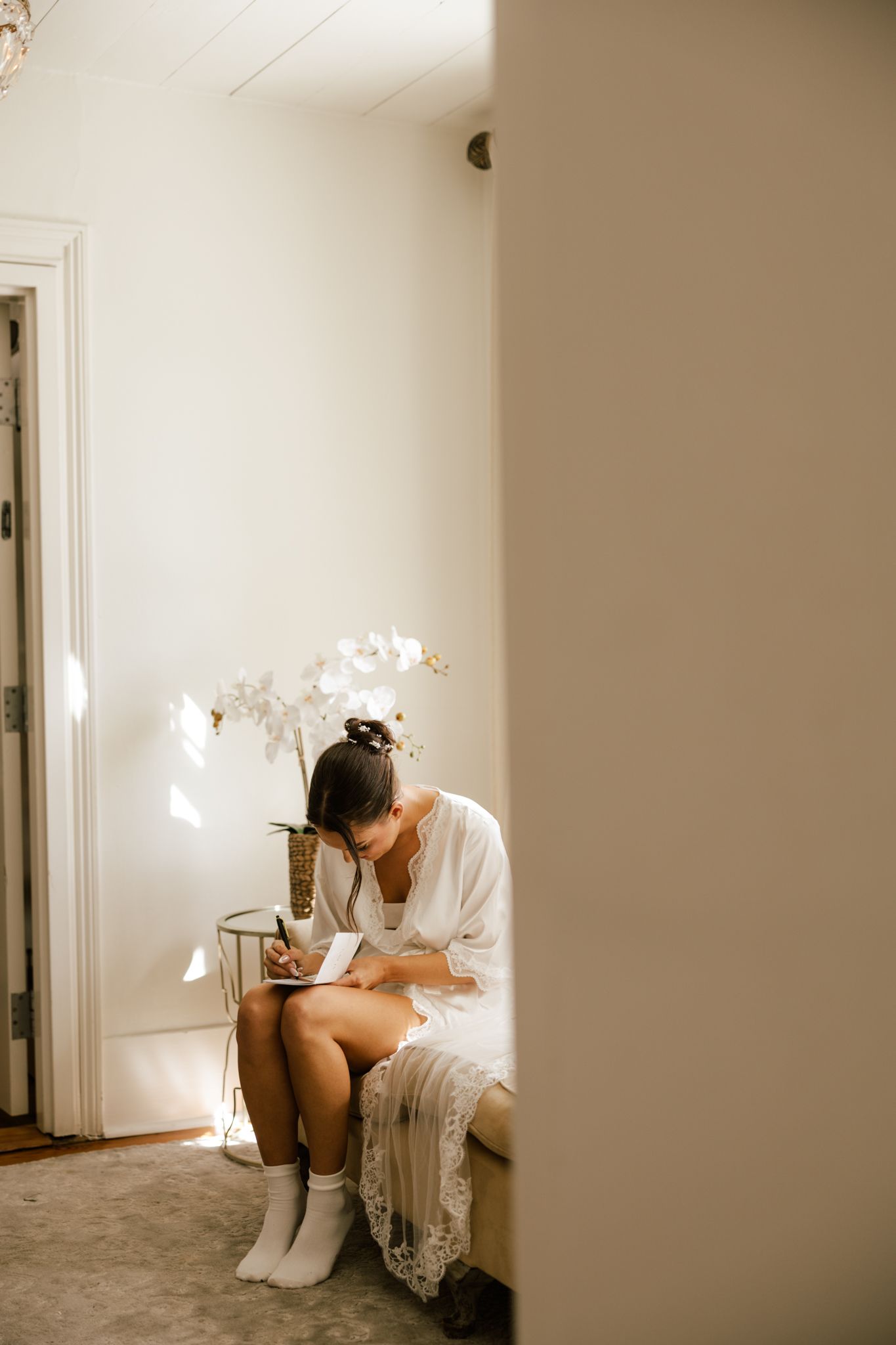 A bride in white sits in a sunlit corner writing in a journal next to white flowers in Duluth Georgia