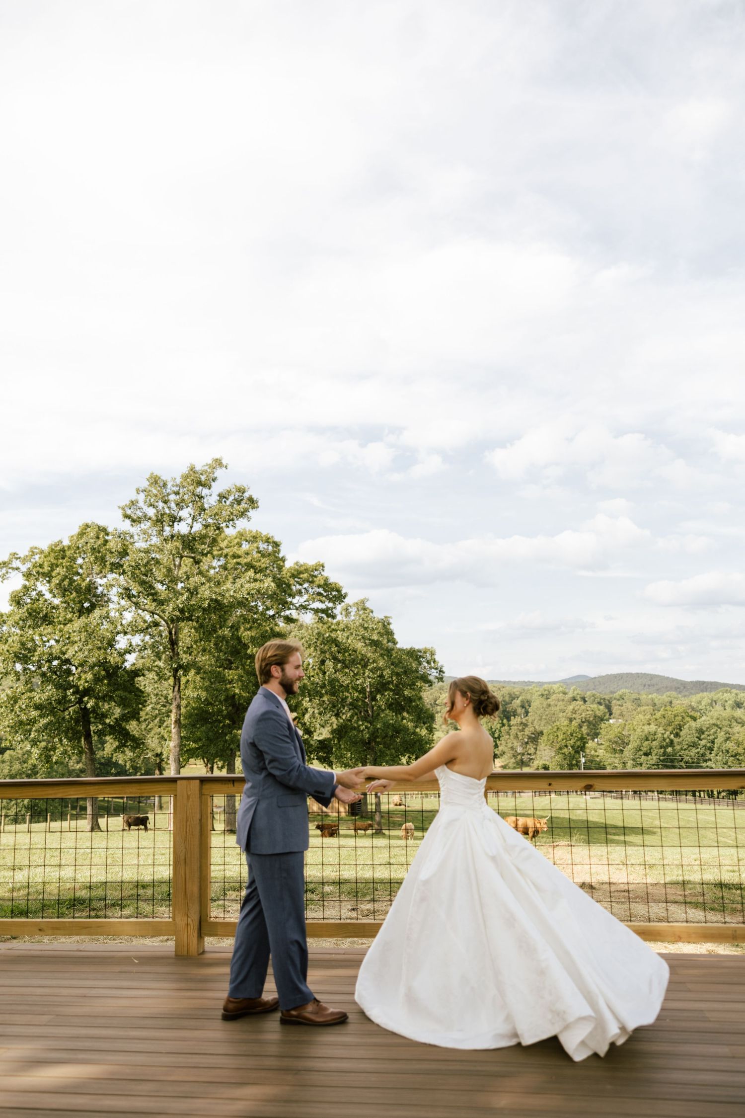 Bride and groom dance on outdoor deck with scenic countryside views and rolling hills in the background on their wedding day.