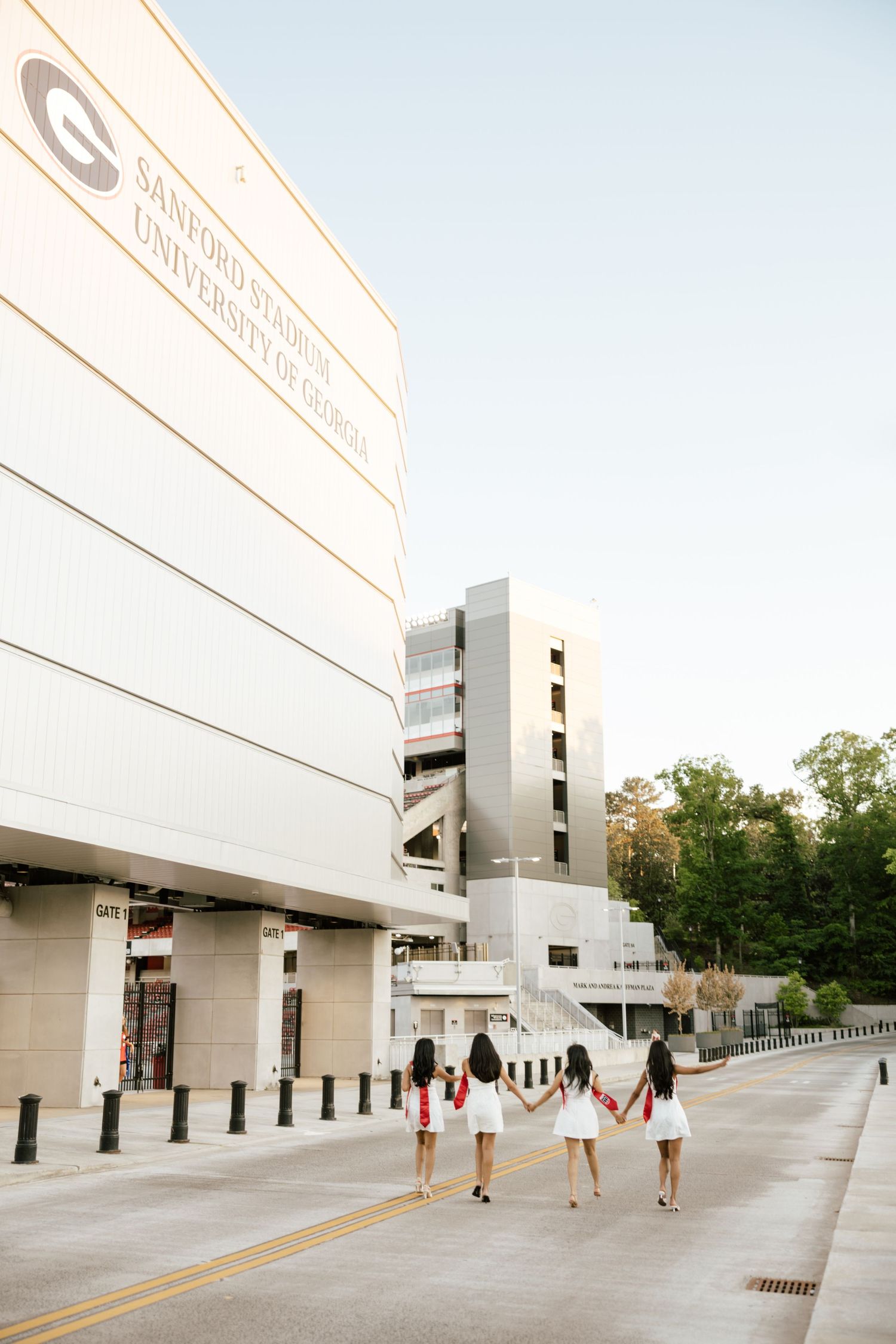 Four women in white dresses hold hands walking toward Sanford Stadium at the University of Georgia.