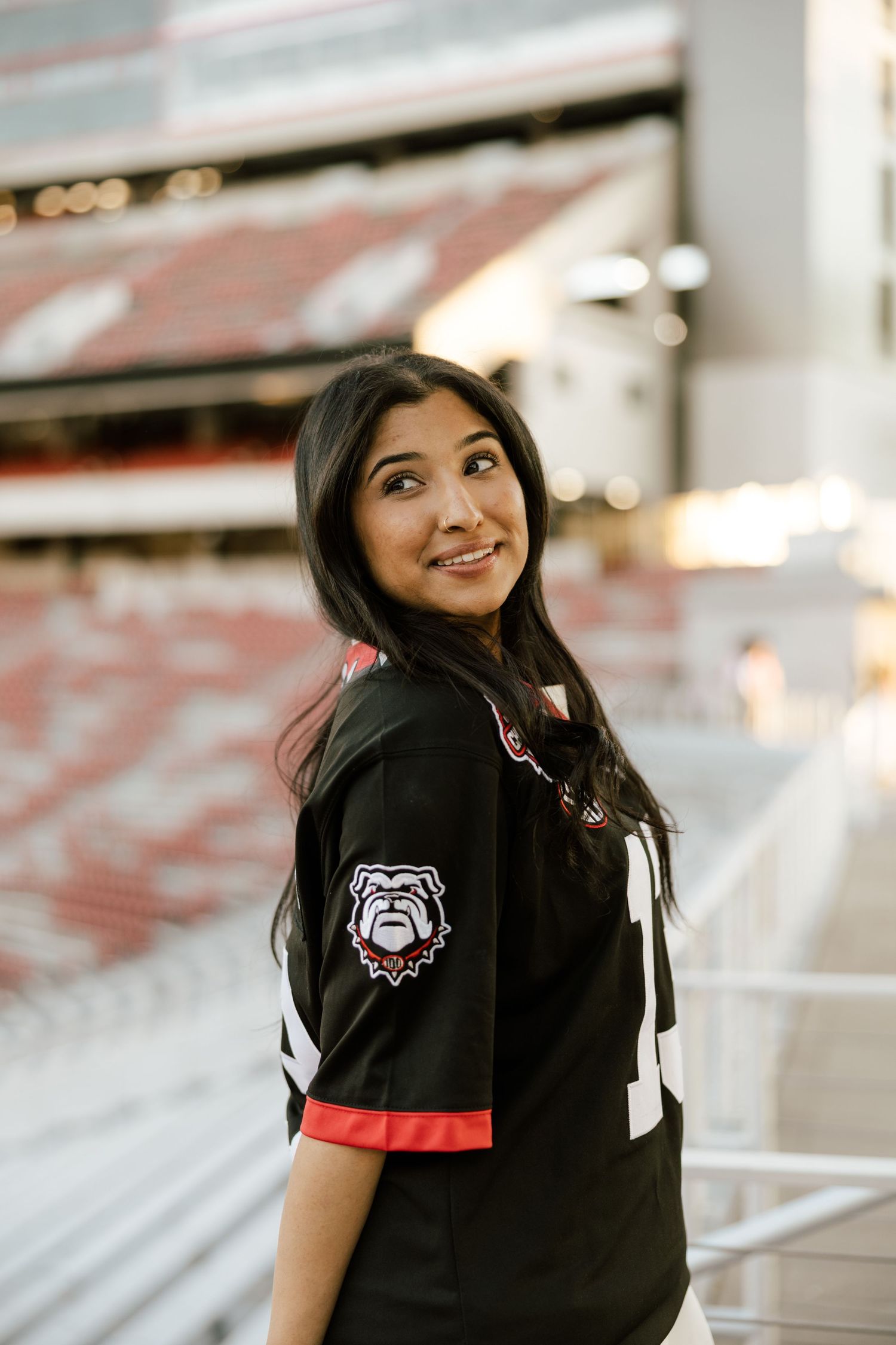 Young woman smiling in a Georgia Bulldogs black jersey at Sanford Stadium, looking over her shoulder.