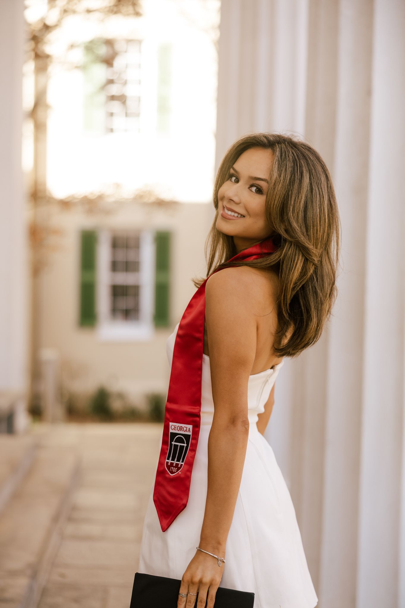 White dress with red sash captured in sunlit corridor with classical columns.